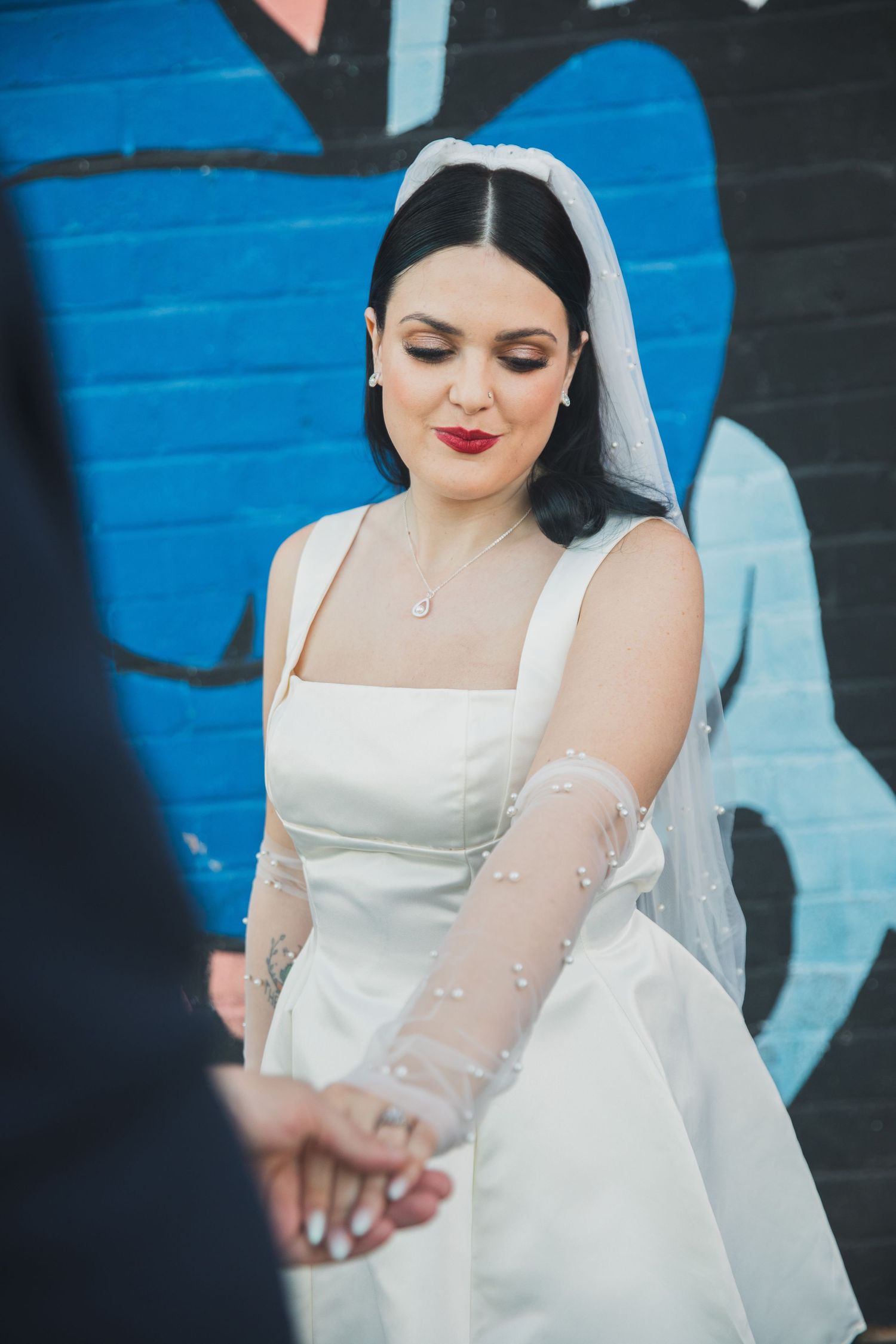 Elegant bride in a white dress with veil smiles while looking down during her wedding day.