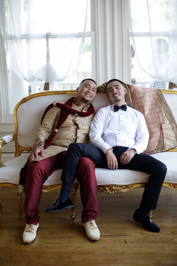 Two people relaxing on an elegant vintage-style couch in formal wedding attire.