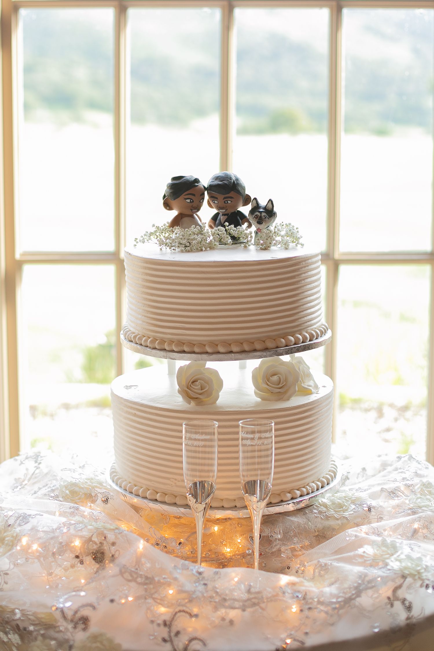 Elegant two-tier white wedding cake with decorative toppers on display with twinkle lights.