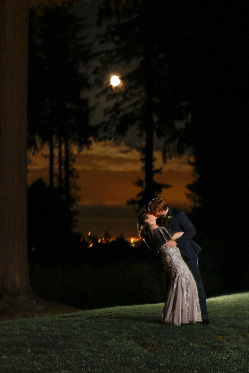 Romantic sunset silhouette of a couple dancing on a grassy hill.