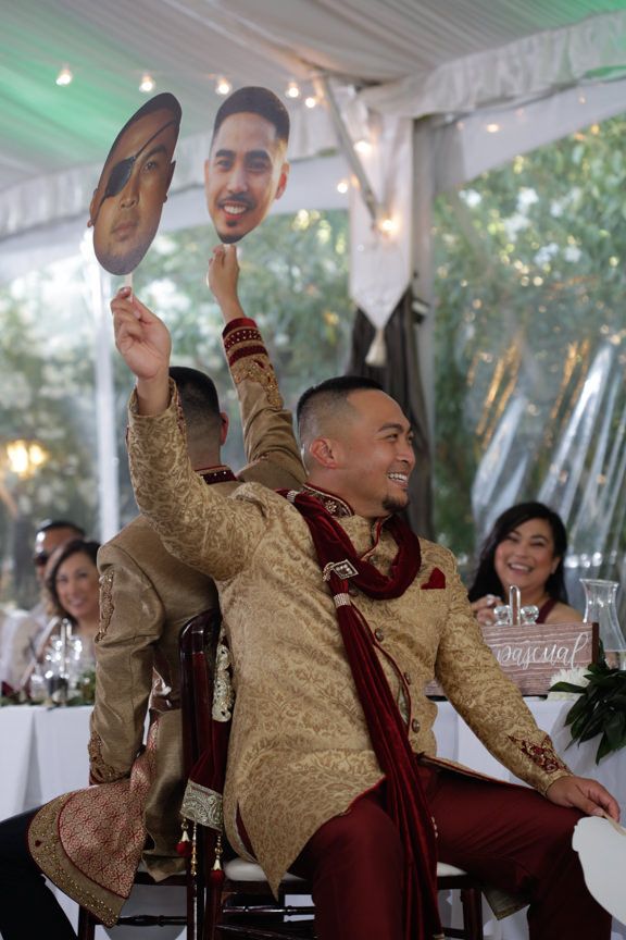 Groomsmen celebrate at a wedding reception wearing matching burgundy suits and gold jackets.