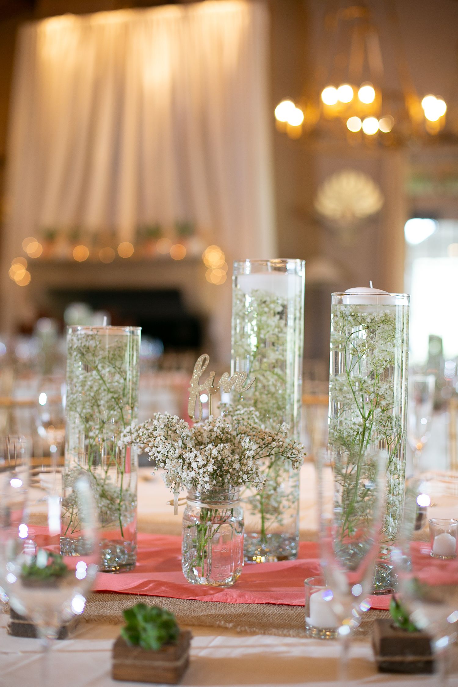 Wedding centerpiece with tall glass vases filled with baby's breath and soft glowing candlelight.
