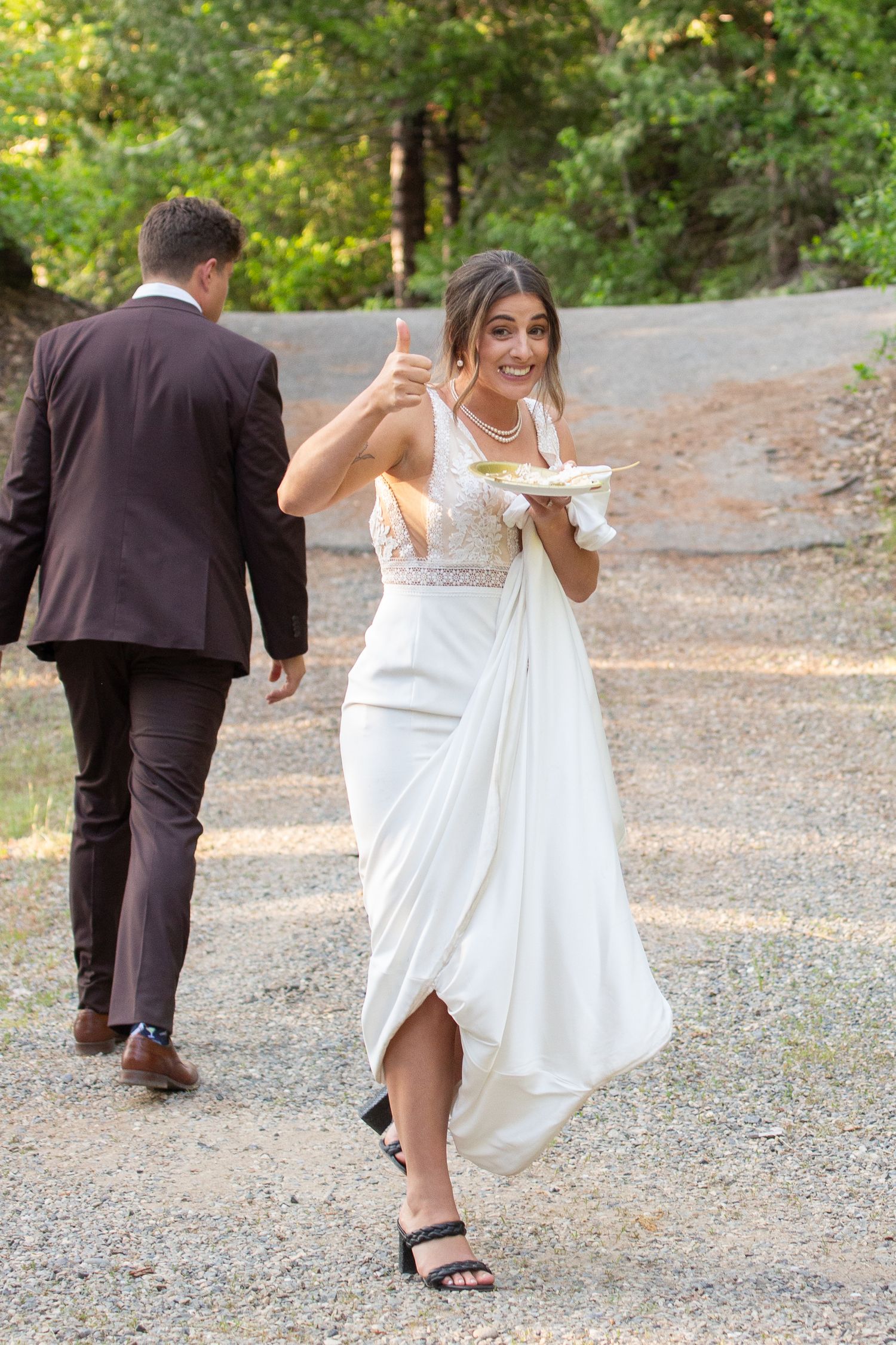 Wedding party members walk along forest path in formal attire.