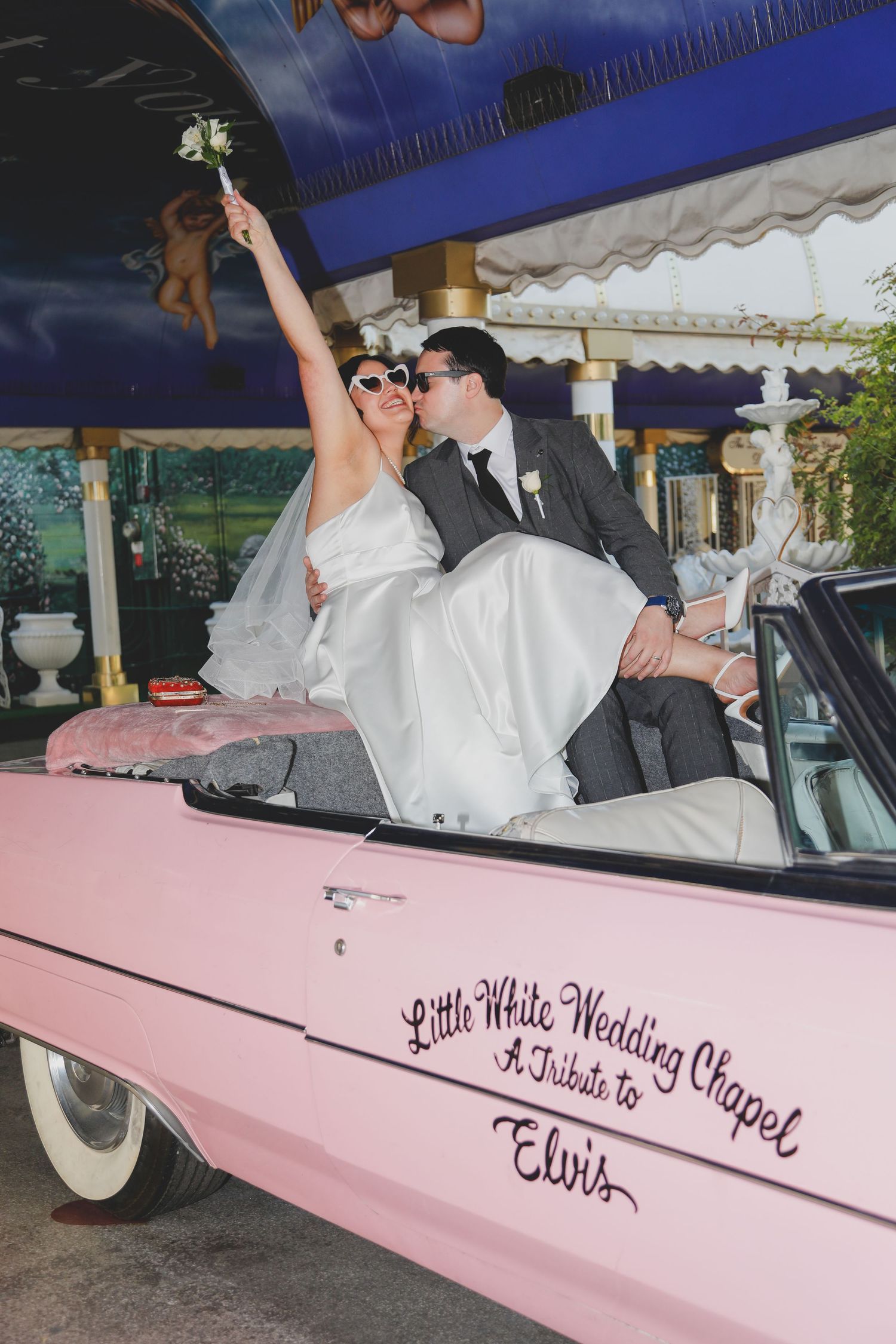 Newlyweds posing in classic pink vintage car with wedding signage.
