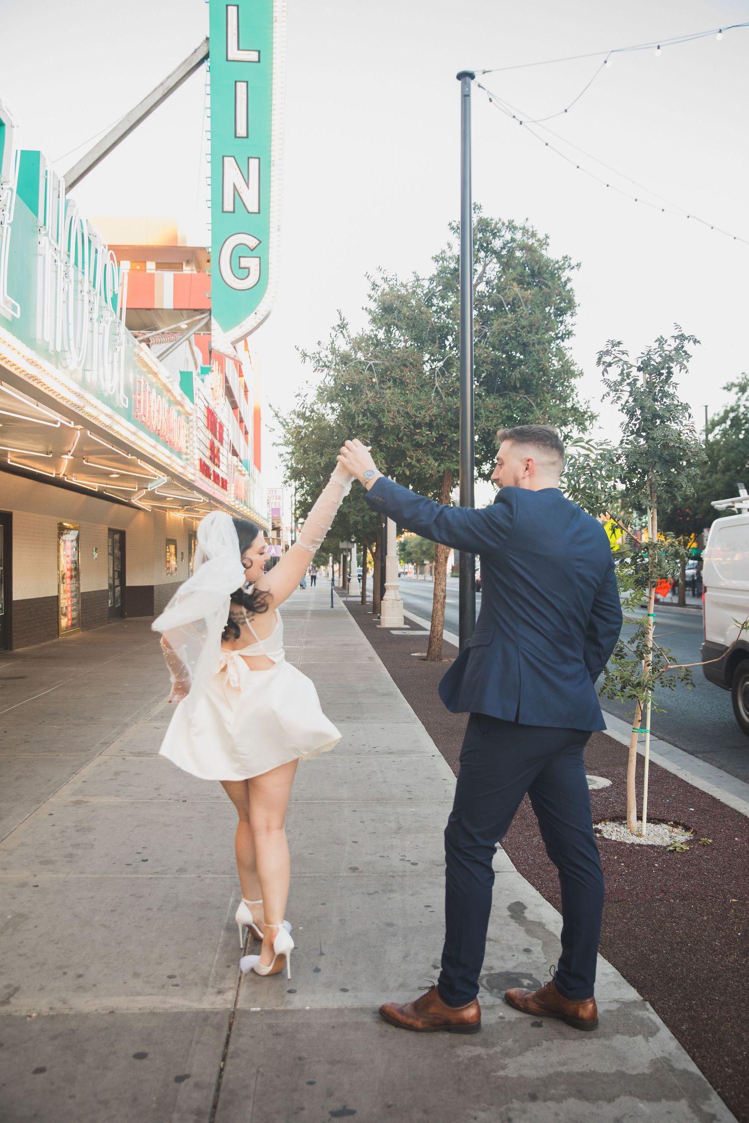 Couple dancing and twirling under vintage signage on their wedding day.