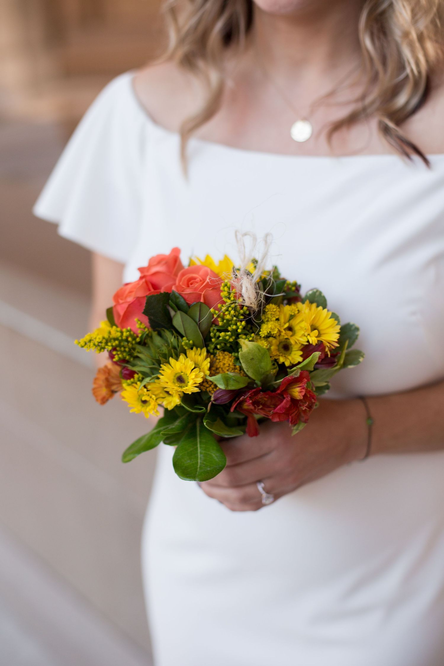 Bright yellow and orange wildflower bouquet held against white dress.