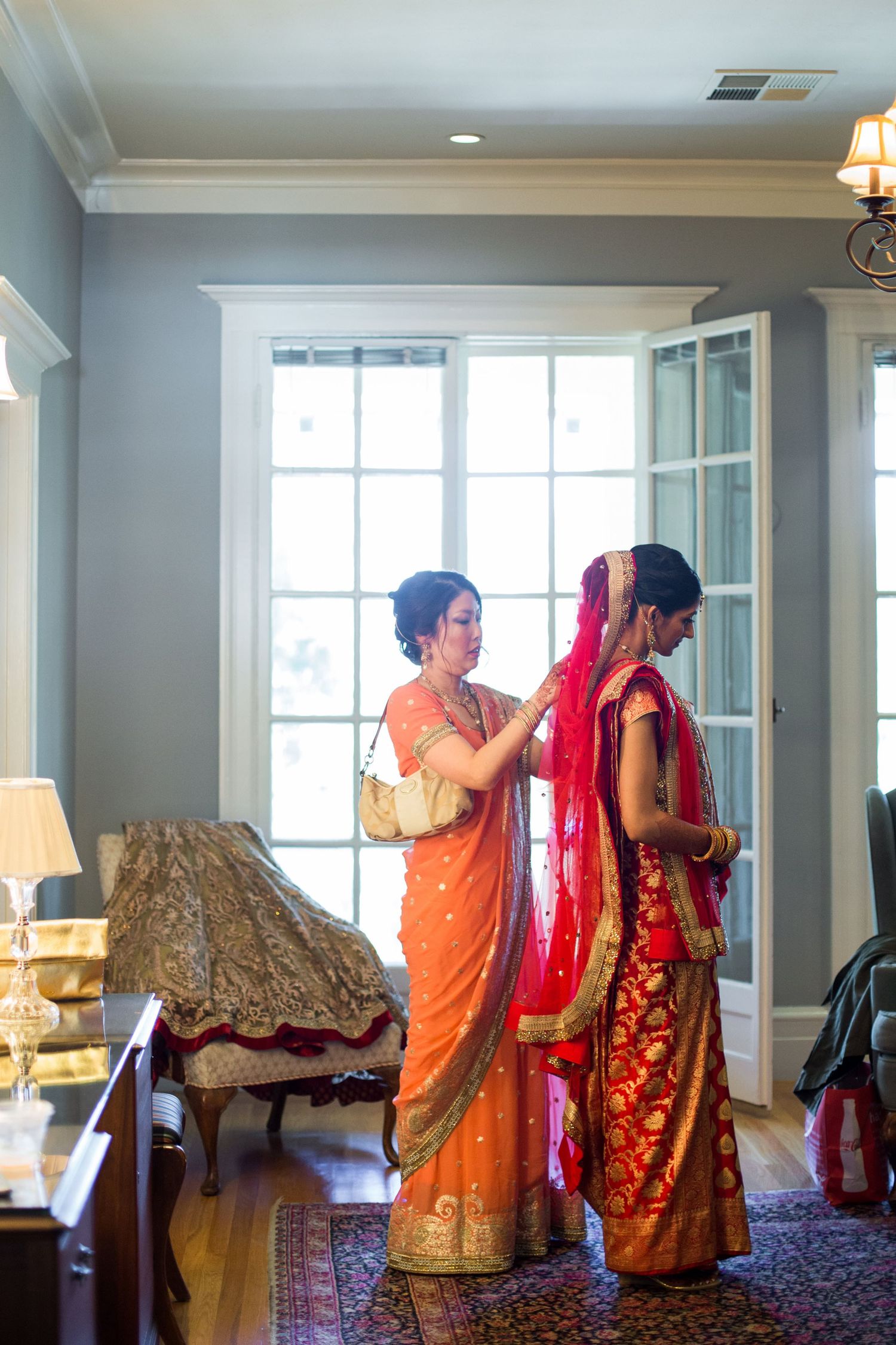 Wedding preparation scene with orange and red saris against blue walls and elegant furniture.