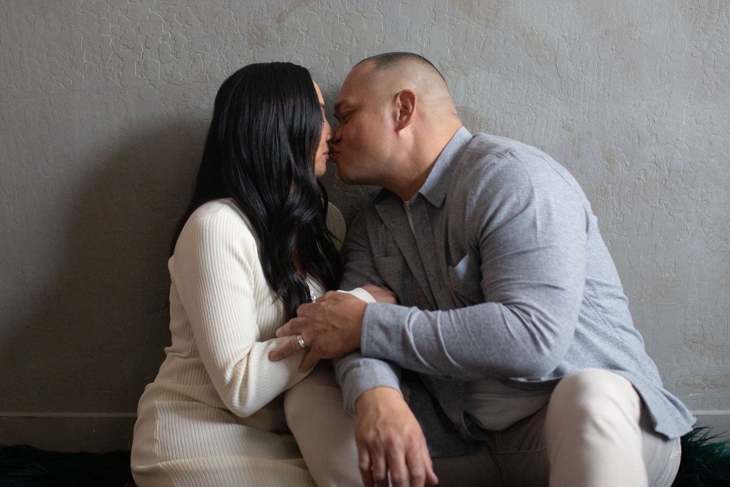 Intimate moment between couple sitting together against neutral wall.