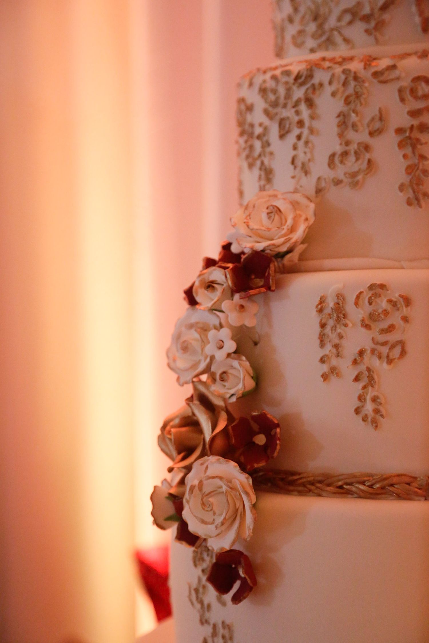 Close-up of intricate floral details on a wedding cake with soft pink lighting.