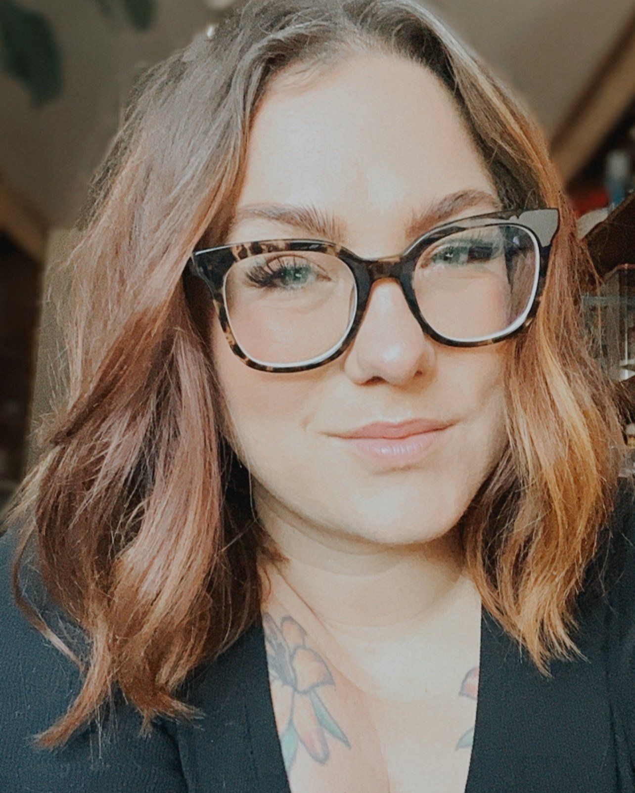 Professional portrait of a person wearing tortoise shell glasses and black blazer with wavy brown hair.
