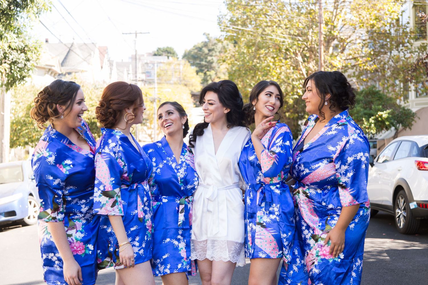 Bridal party in matching blue floral robes poses together outdoors on wedding day.