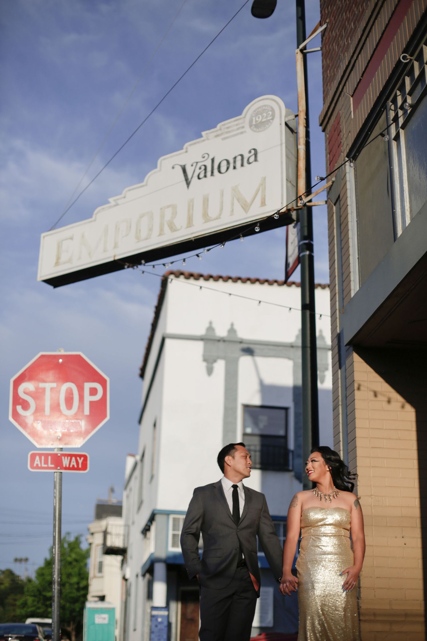 A vintage-style shot of a couple beneath the Valona Emporium sign and stop sign.