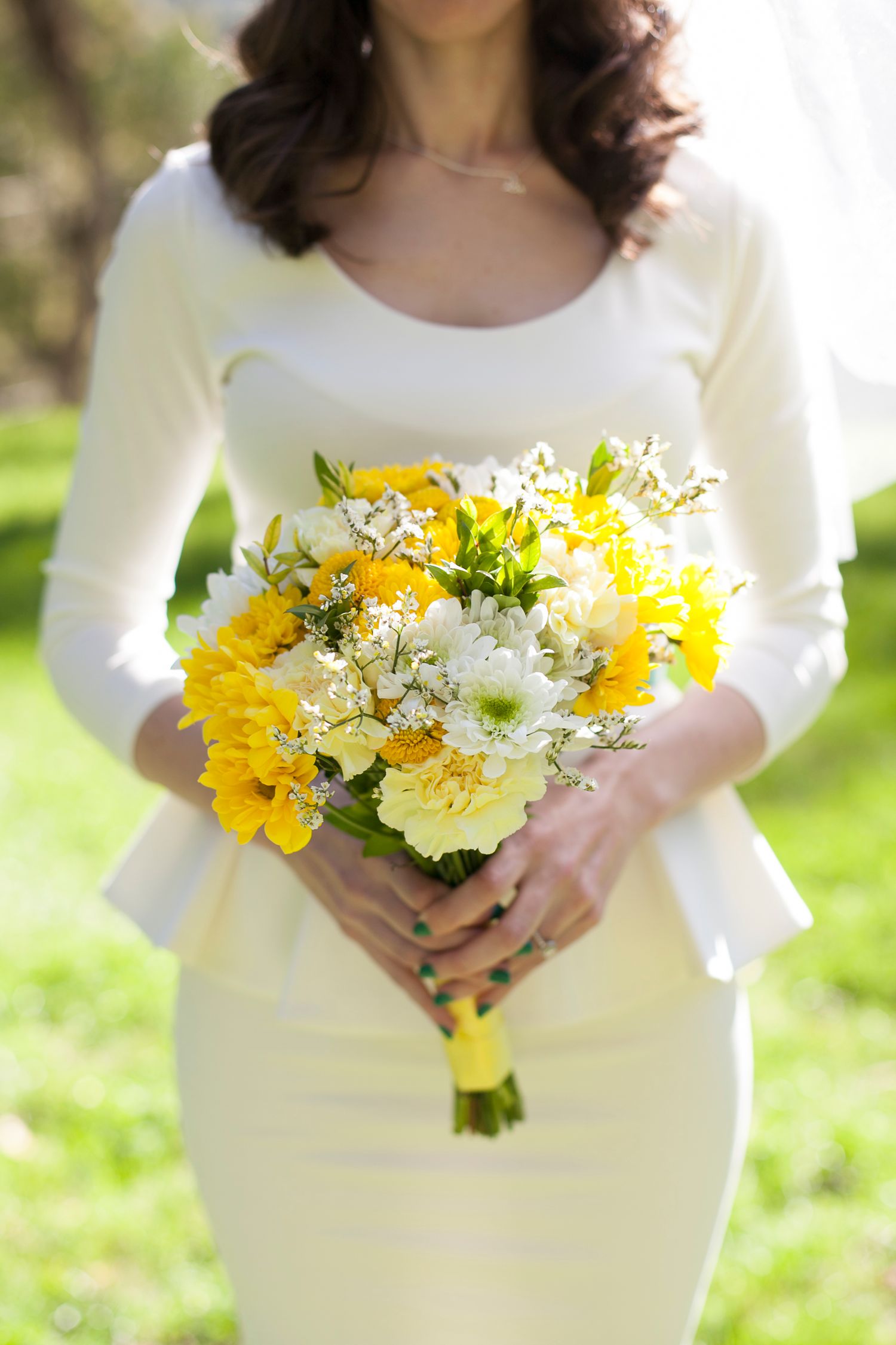 Yellow and white flower bouquet held against a white dress in an outdoor garden setting.
