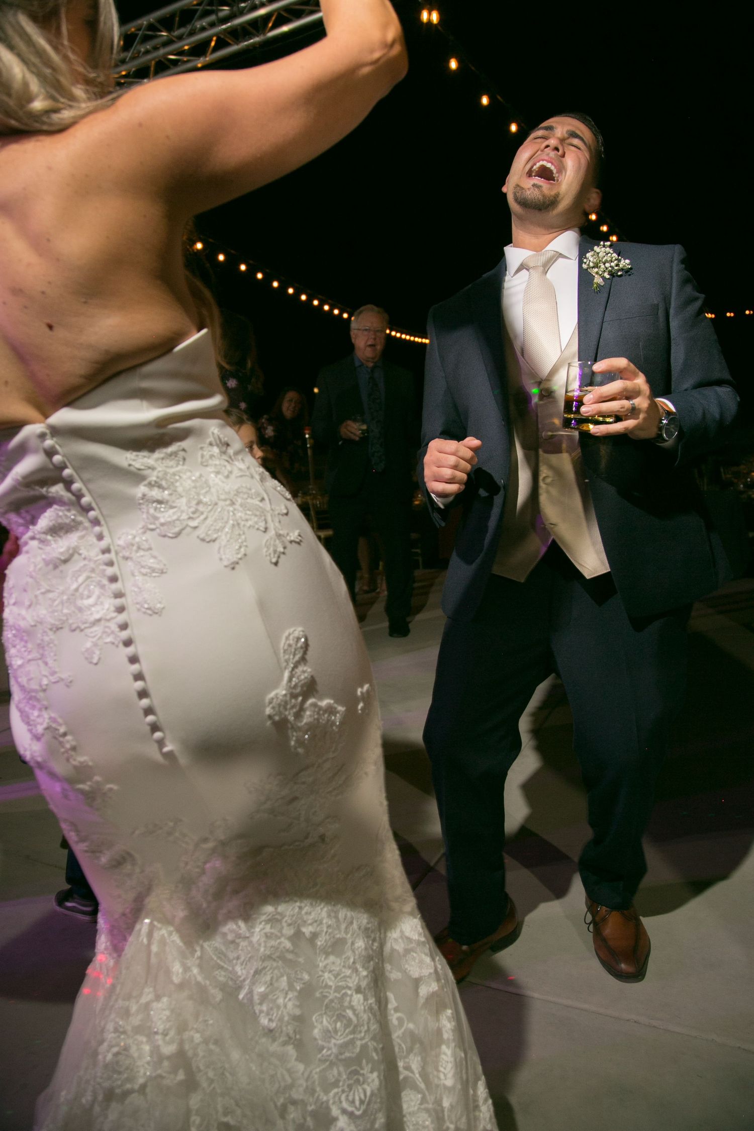 Dancing couple celebrating at wedding reception under twinkling lights.