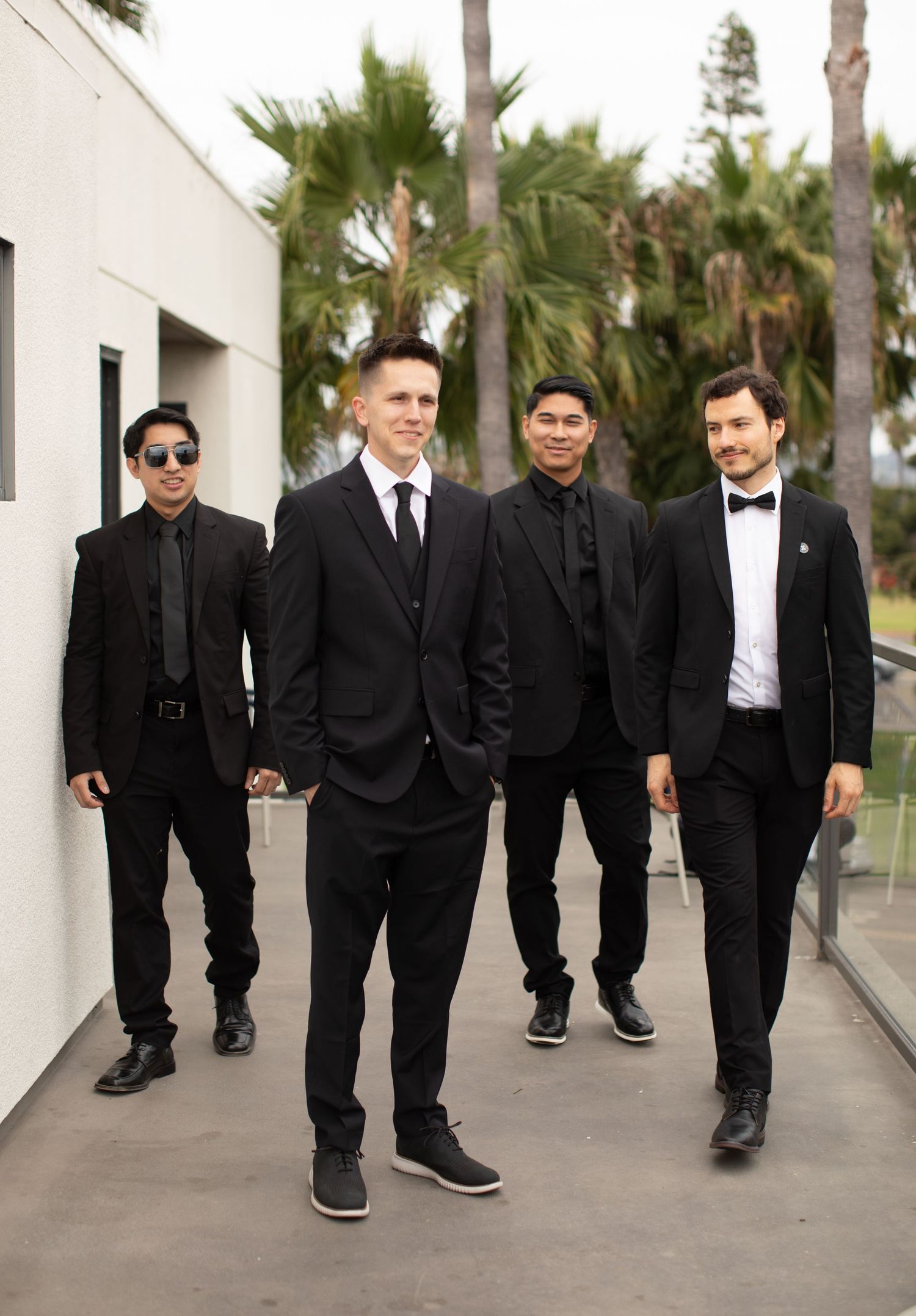 A group of formally dressed people walking together outside a modern building with palm trees.