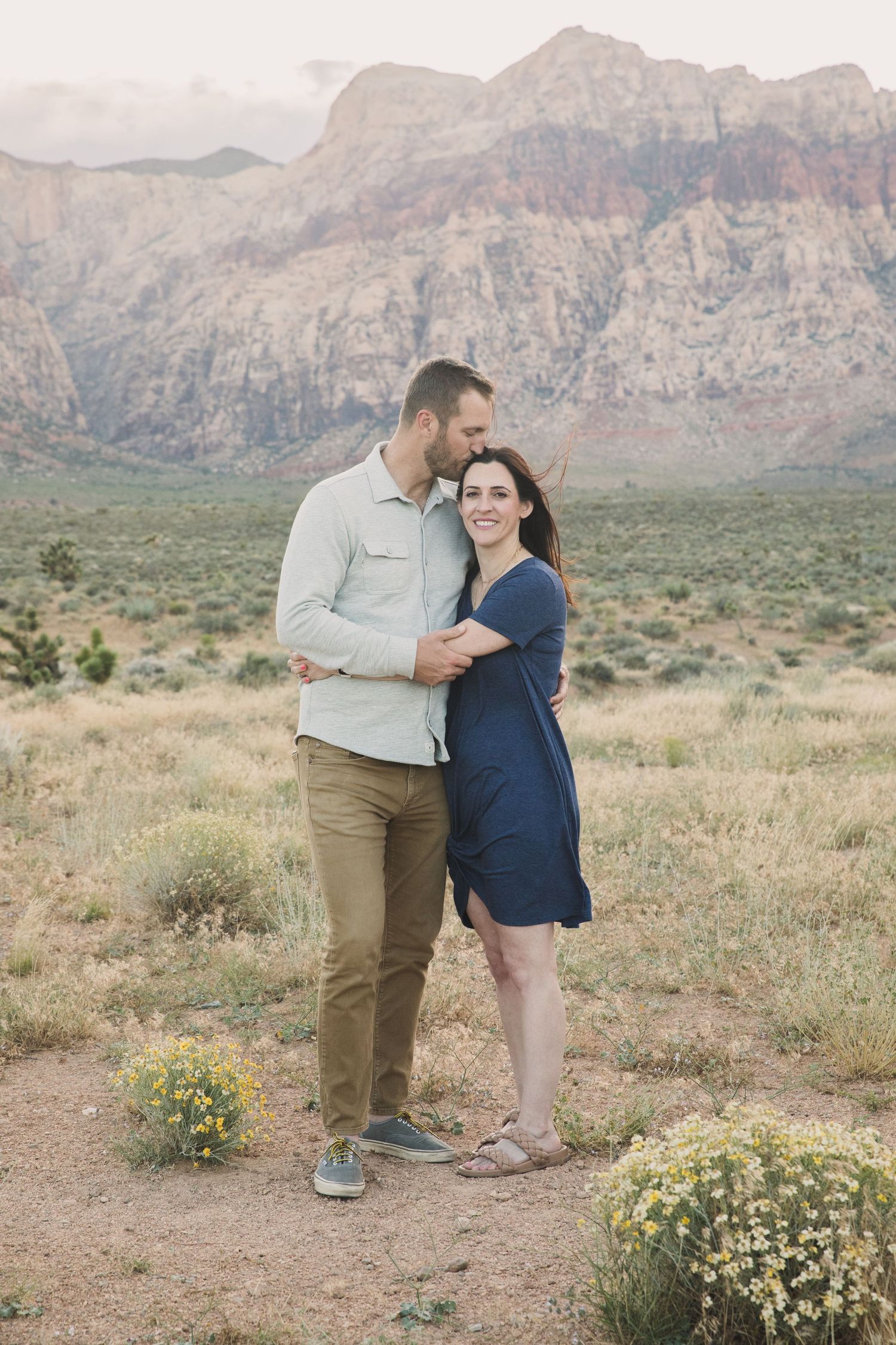 Couple sharing intimate moment in desert landscape with mountains and wildflowers.