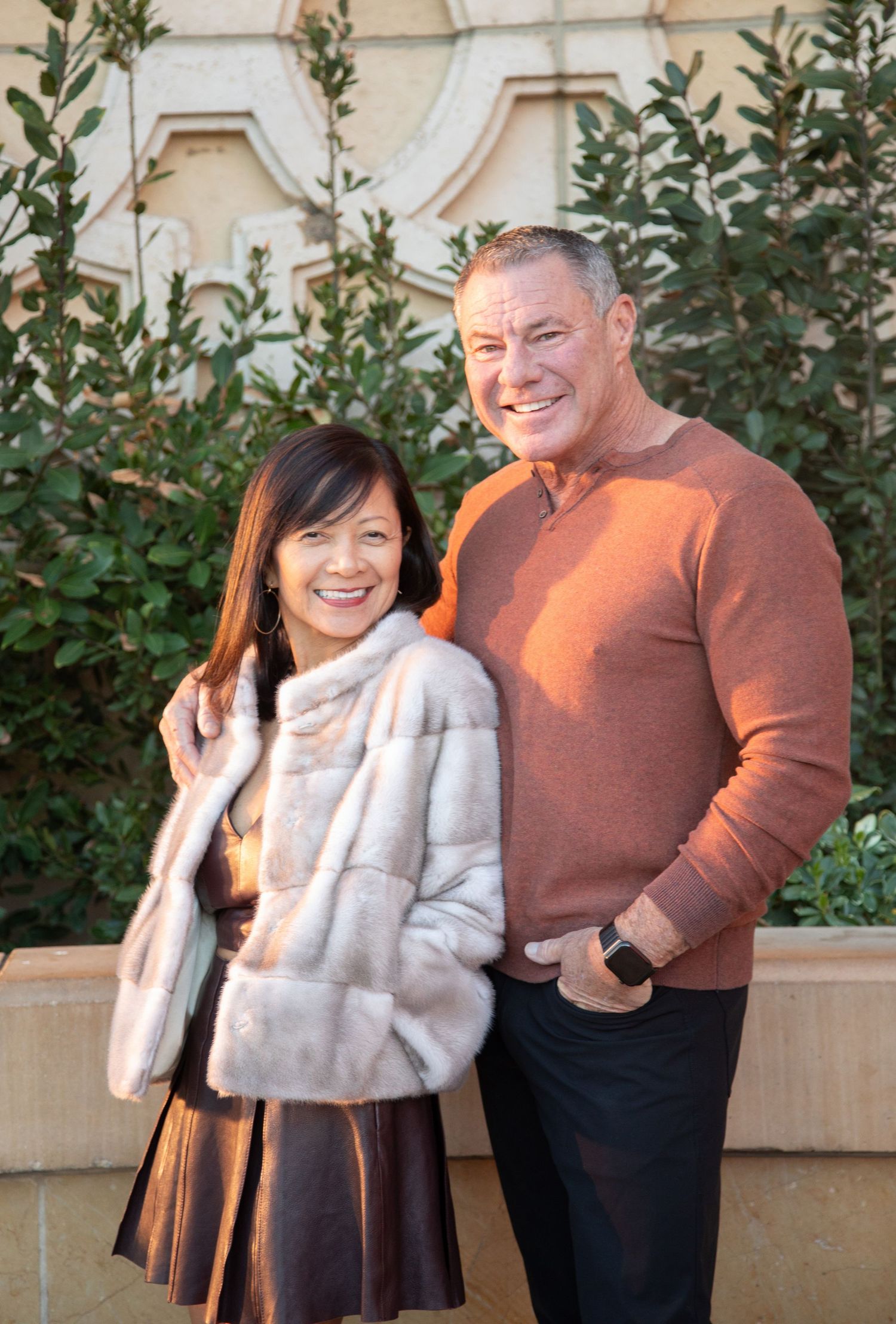Happy couple posing together outdoors against classic building facade with greenery.