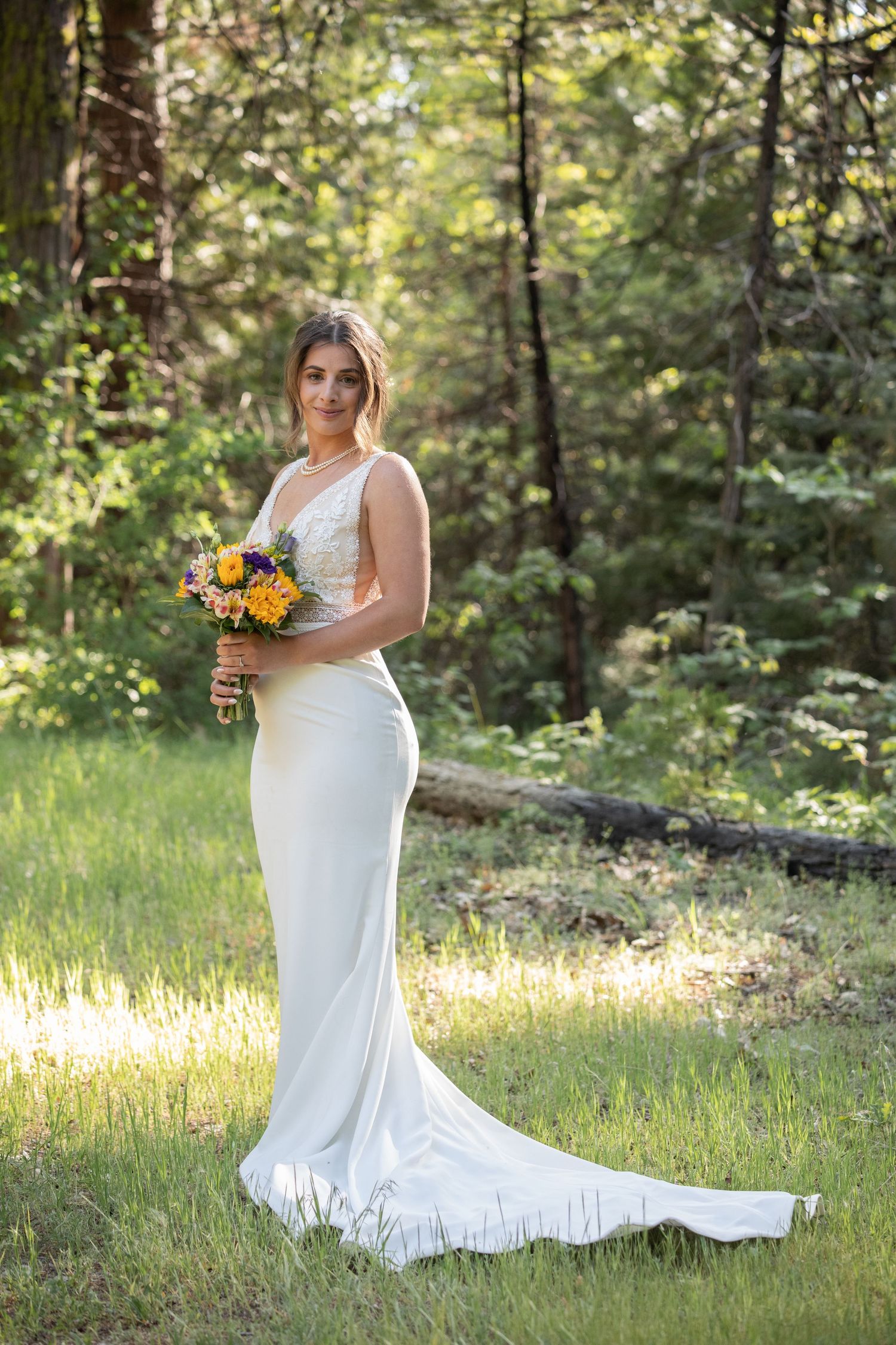 Outdoor bridal portraits in a sunlit forest clearing with yellow wildflower bouquet.