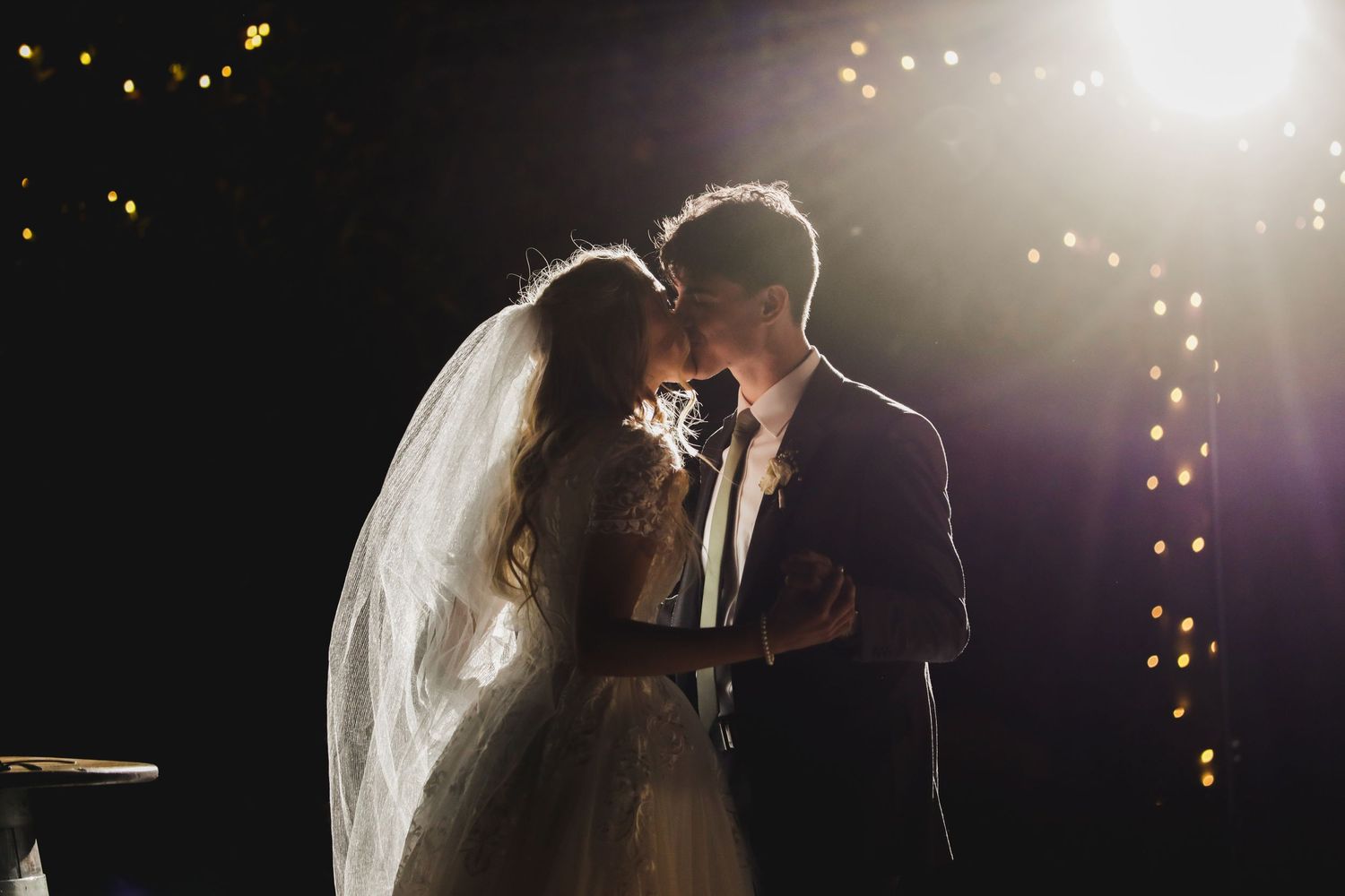 Silhouetted newlyweds share intimate moment under twinkling lights.