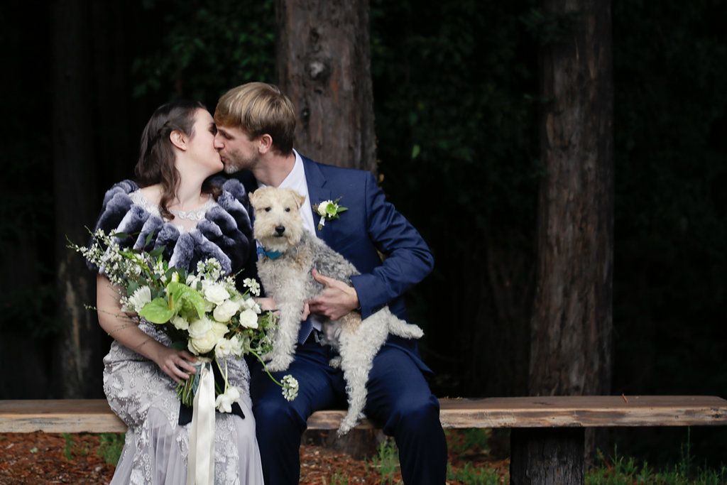 Couple takes romantic wedding photos with their white dog in a wooded setting.