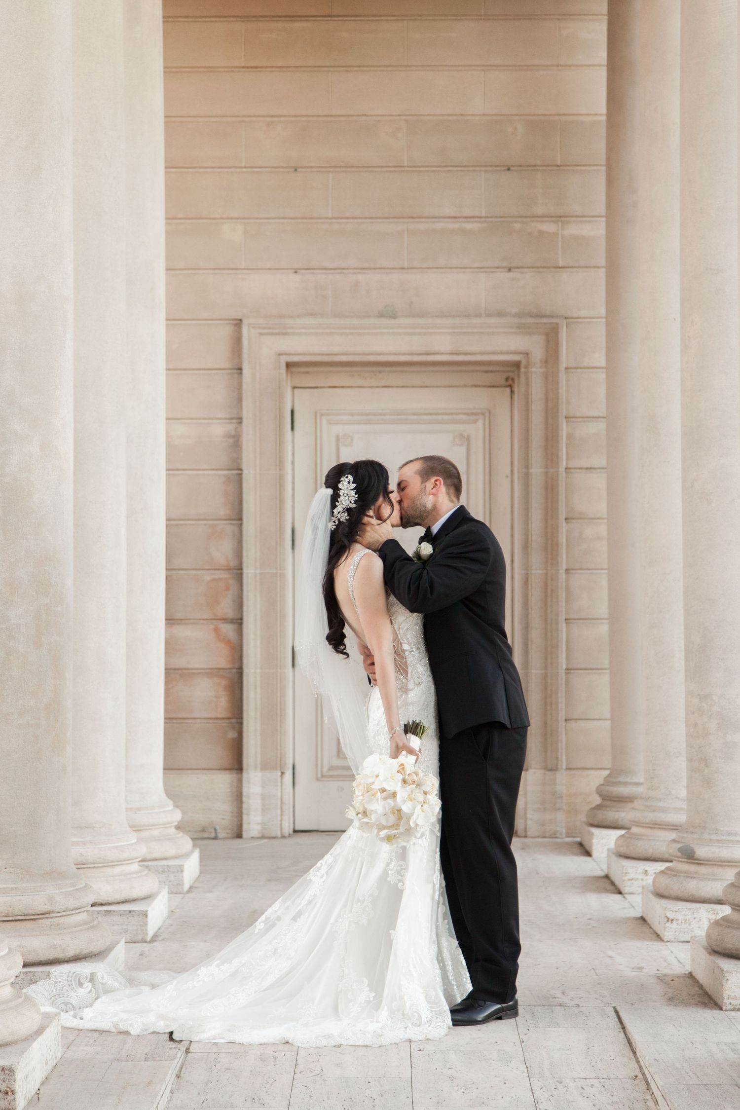 Intimate wedding portrait against cream stone architecture with classical columns.