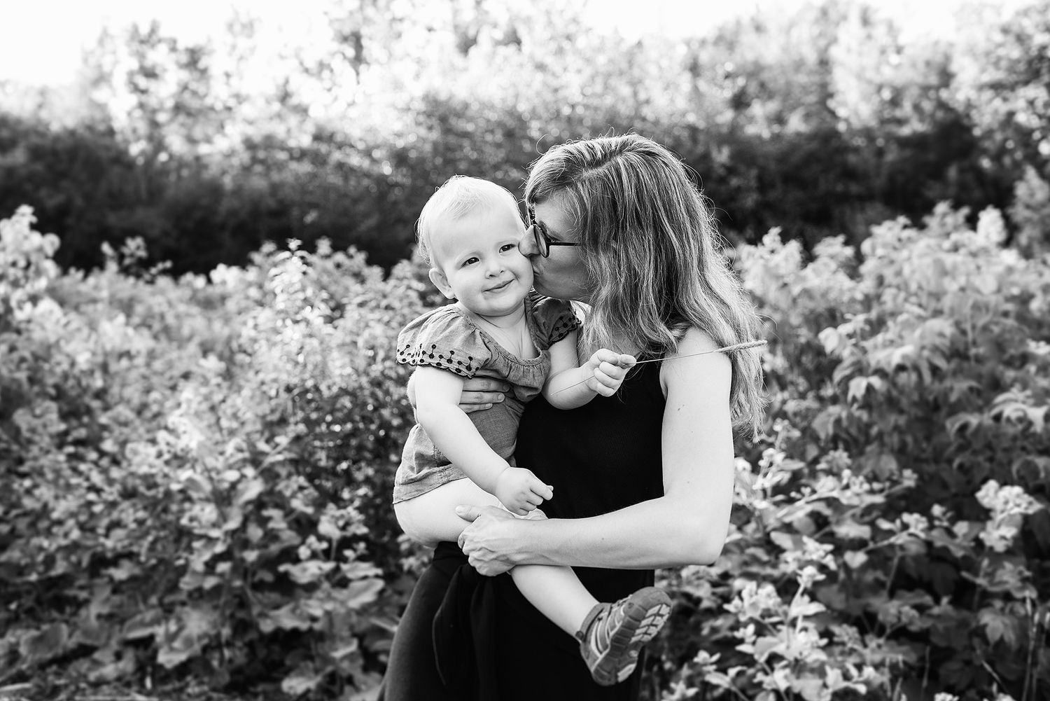 Black and white portrait of loving mother and baby outdoors among wildflowers in nature.