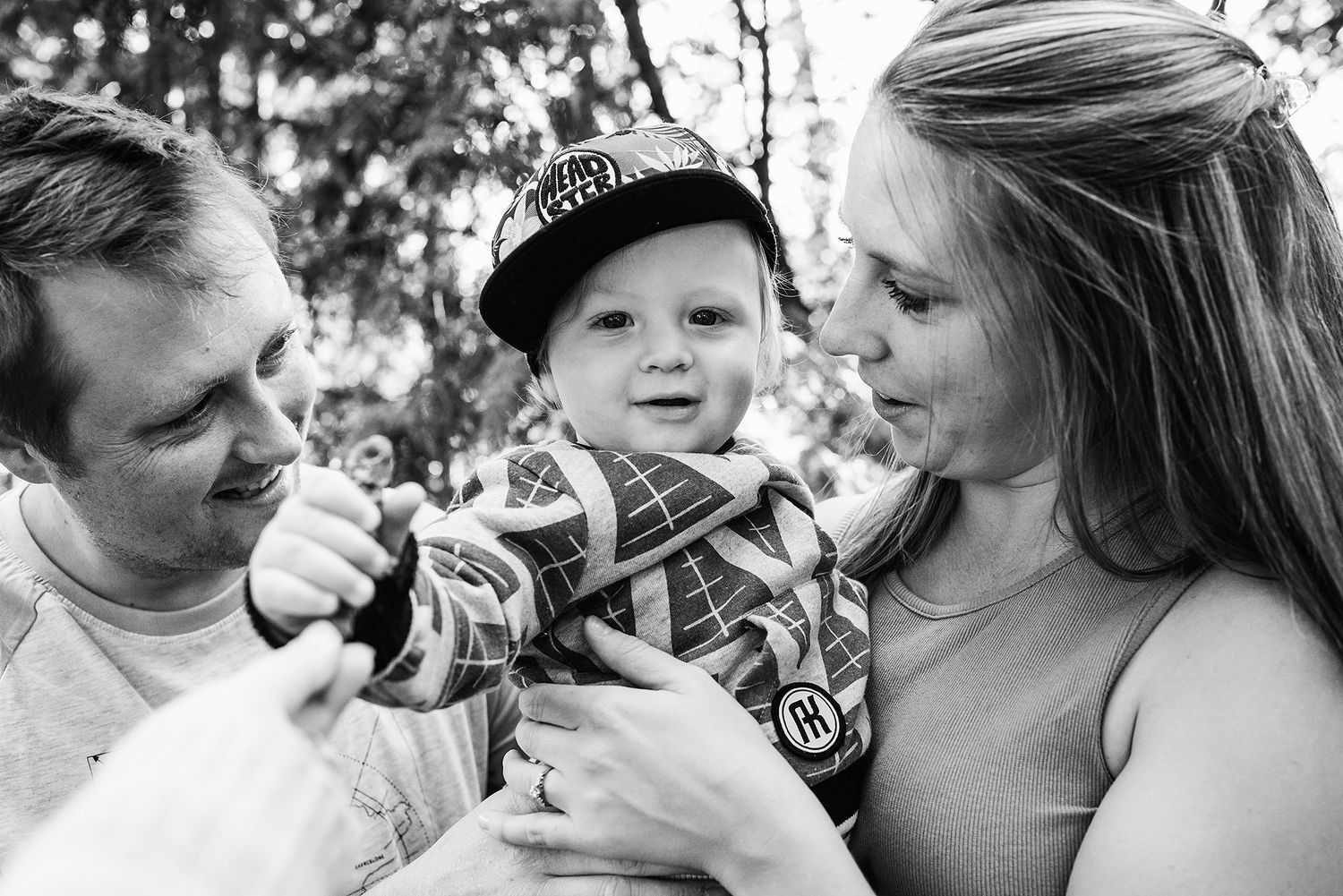 A black and white candid photograph shows family members sharing a moment with a young child in an outdoor setting.