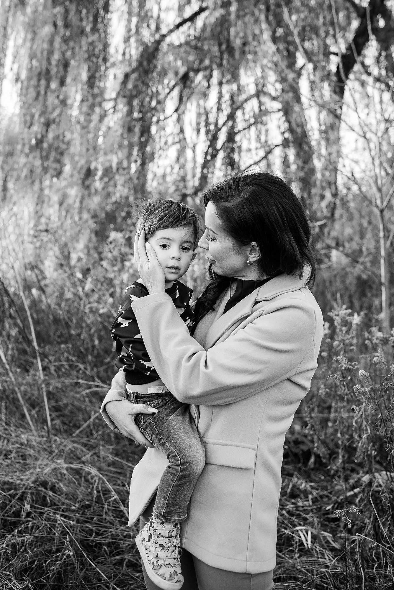 A tender black and white portrait of an adult and child sharing a special moment under weeping willow branches.