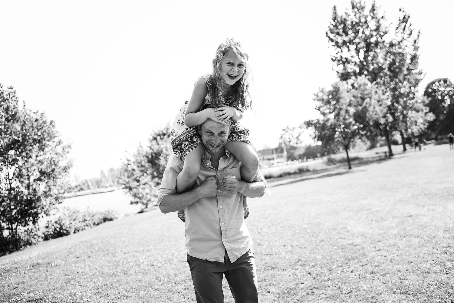 Playful black and white photo of two people enjoying a piggyback ride outdoors in a grassy field.