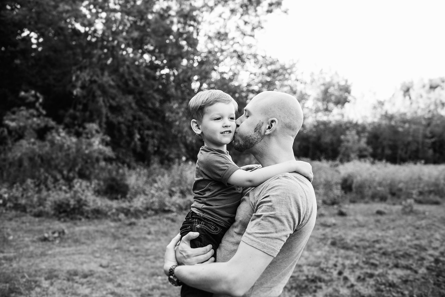 A tender black and white moment outdoors showing a parent holding a young child in their arms.