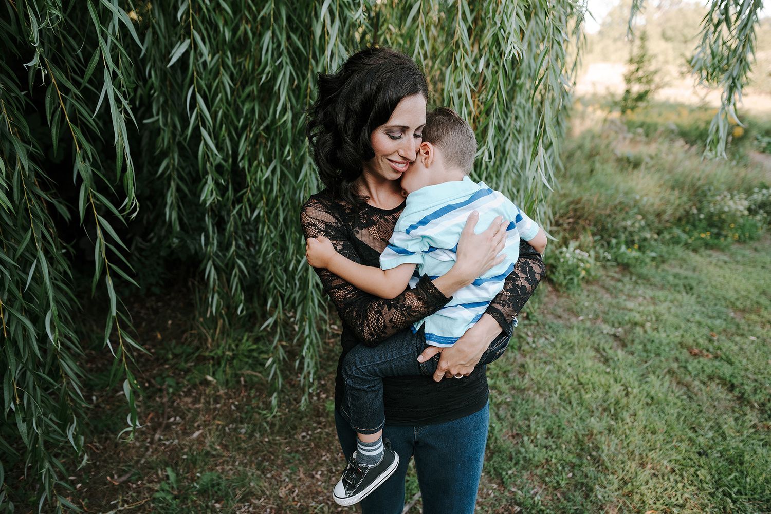 Parent and toddler share a joyful moment together near hanging willow branches in an outdoor setting.