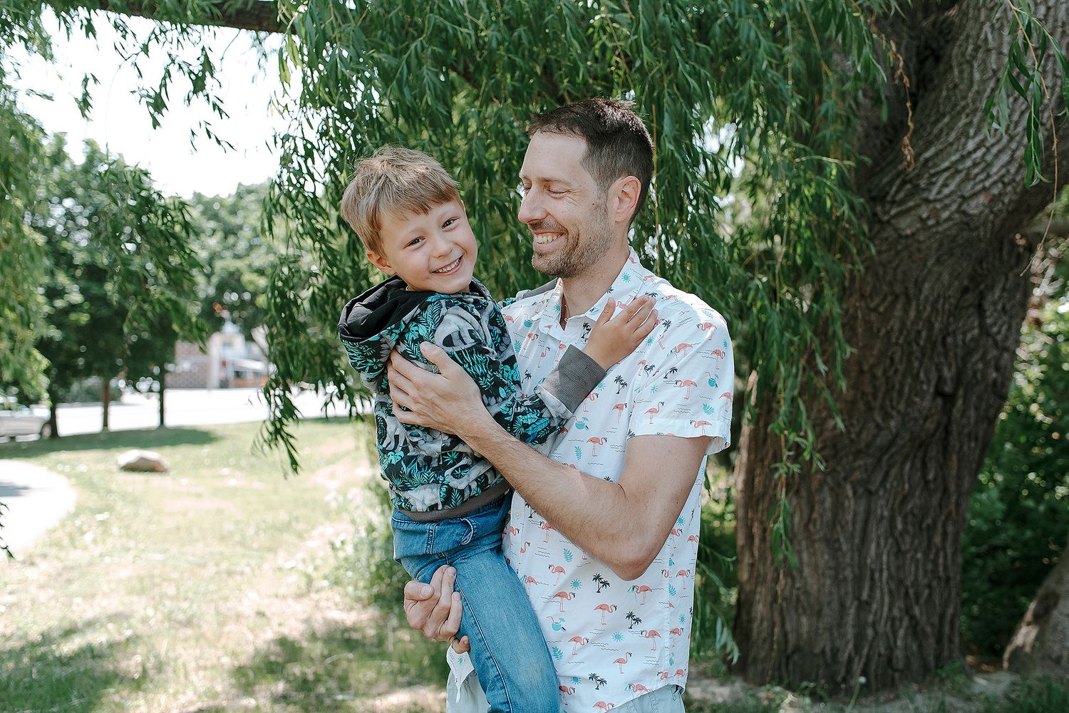 Two figures spend a tender moment together under a willow tree on a bright summer day.