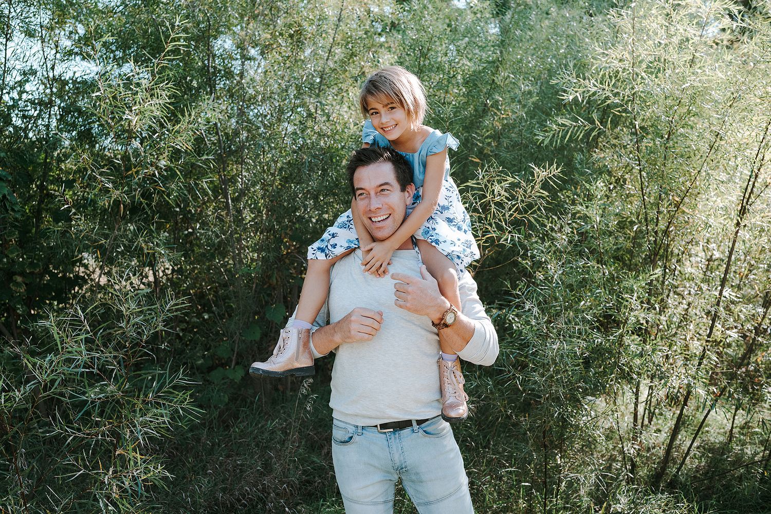 A child sits on an adult's shoulders during an outdoor photo session in a natural green setting.
