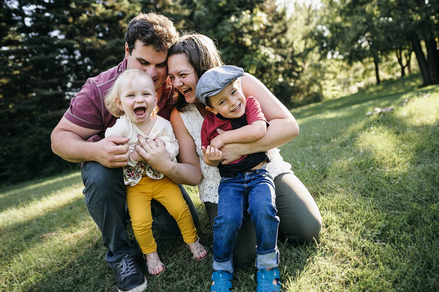 A joyful group sits together outdoors on a grassy hillside during a sunny afternoon, sharing laughter and hugs.