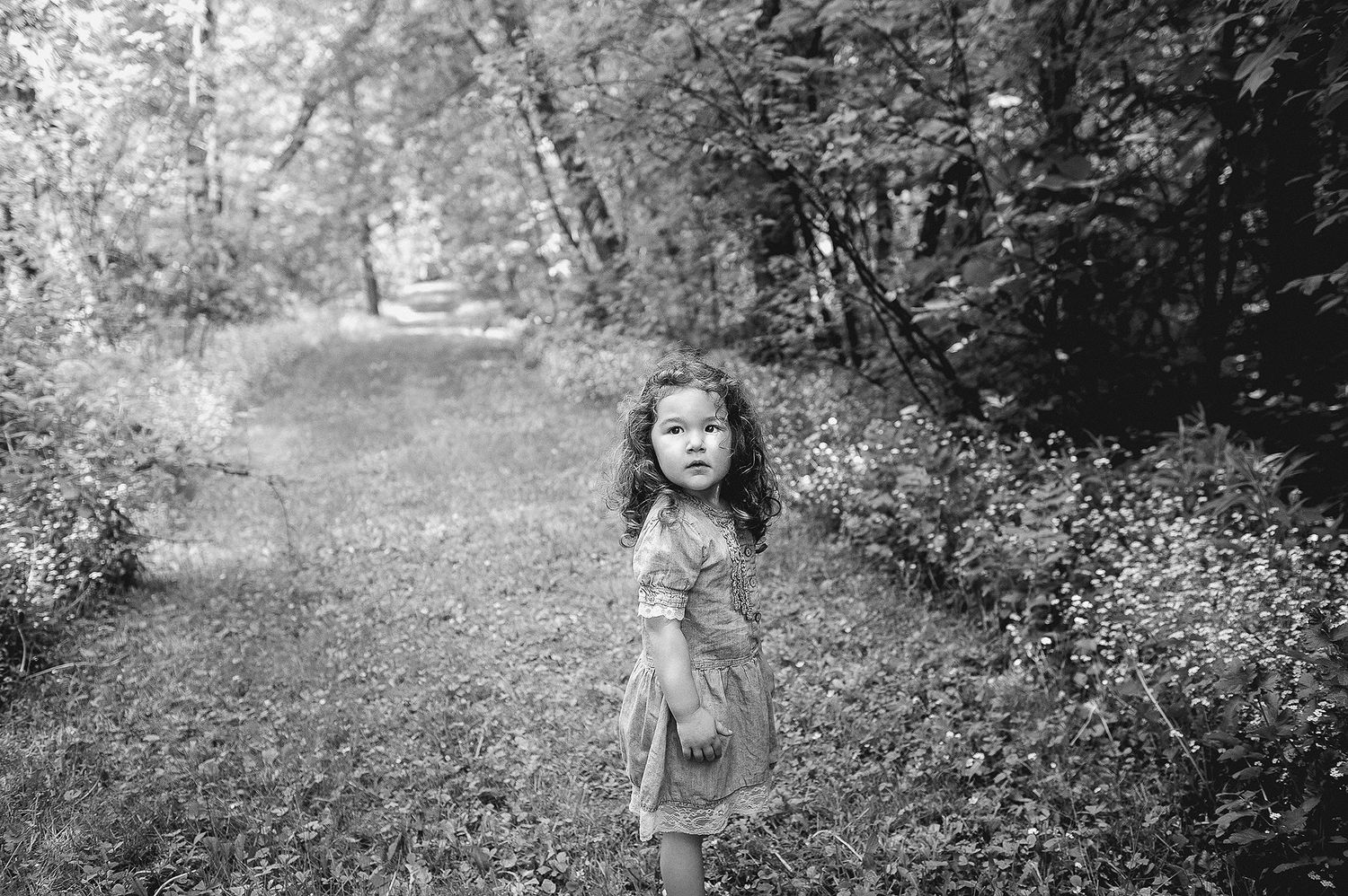 A small child stands on a wooded path in a vintage black and white photograph.
