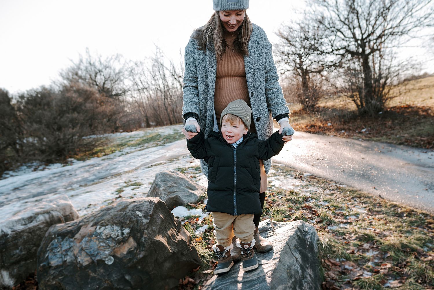 Parent helping small child balance on rocky terrain during winter hike.