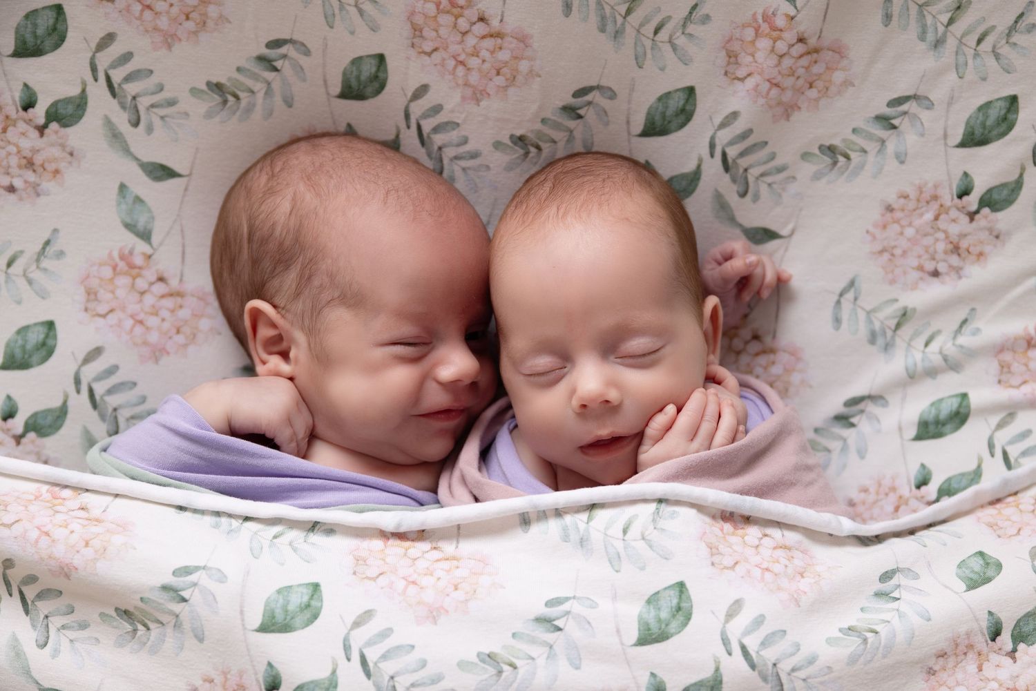 Two sleeping babies lying together on a floral patterned blanket.