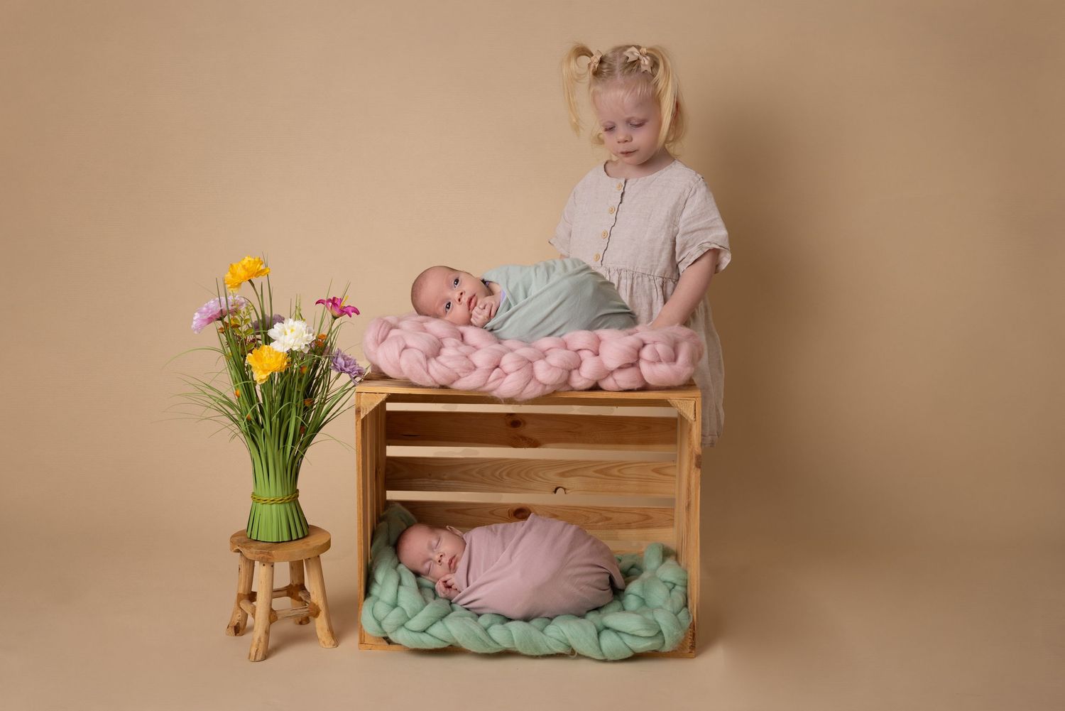A vintage wooden changing table setup with flowers and soft pastel mint and pink fabrics in a studio setting.