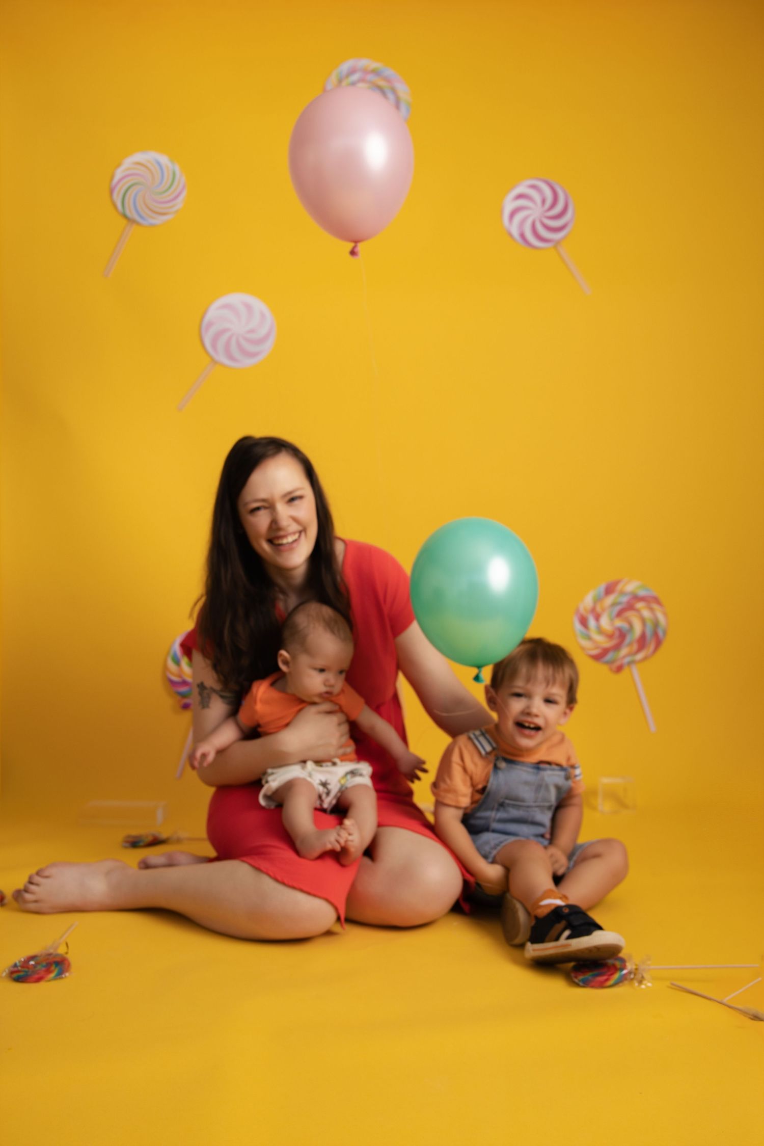 Cheerful family portrait with lollipop decorations and balloons against vibrant yellow backdrop.