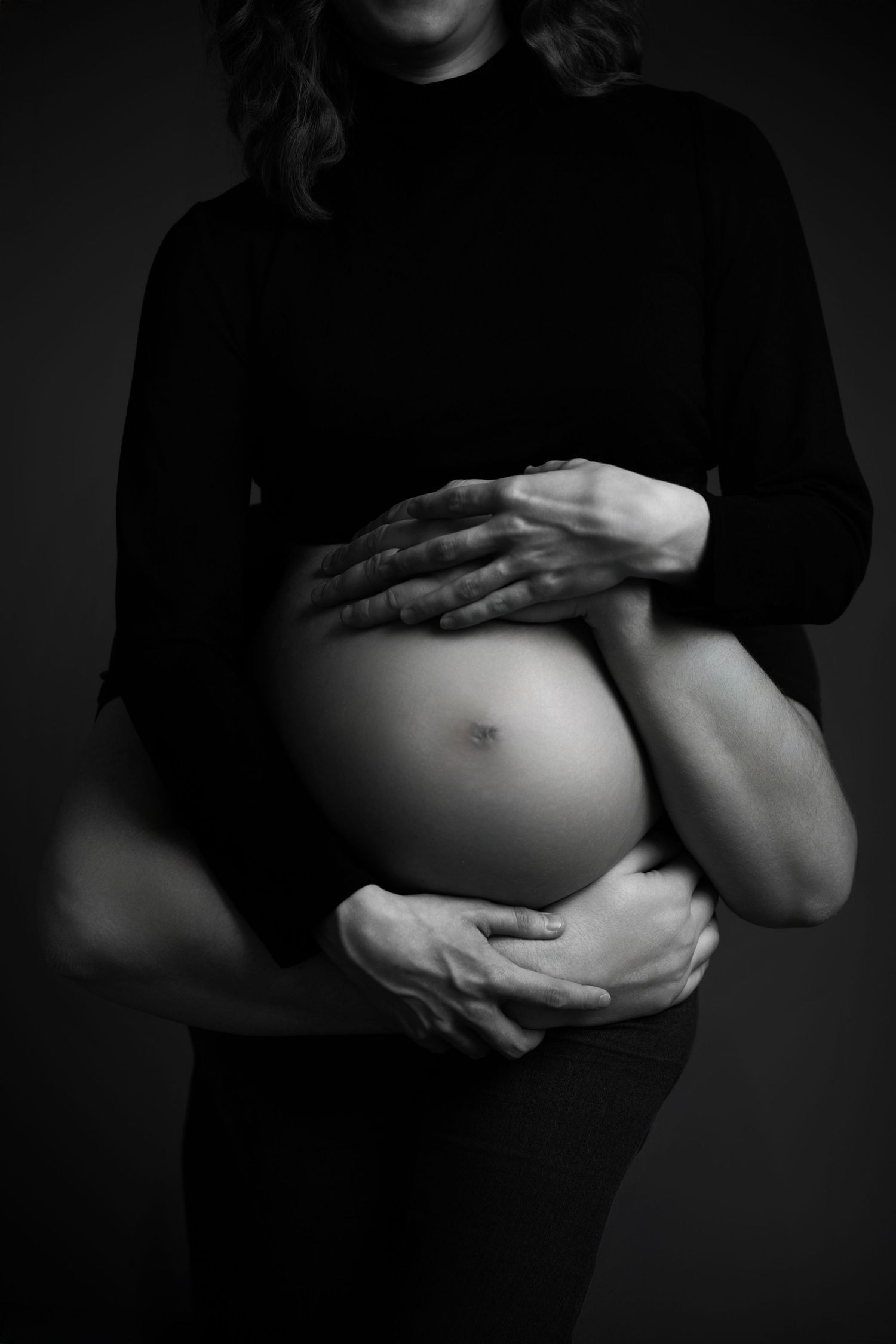 Artistic black and white maternity photo showing hands cradling a pregnant belly.
