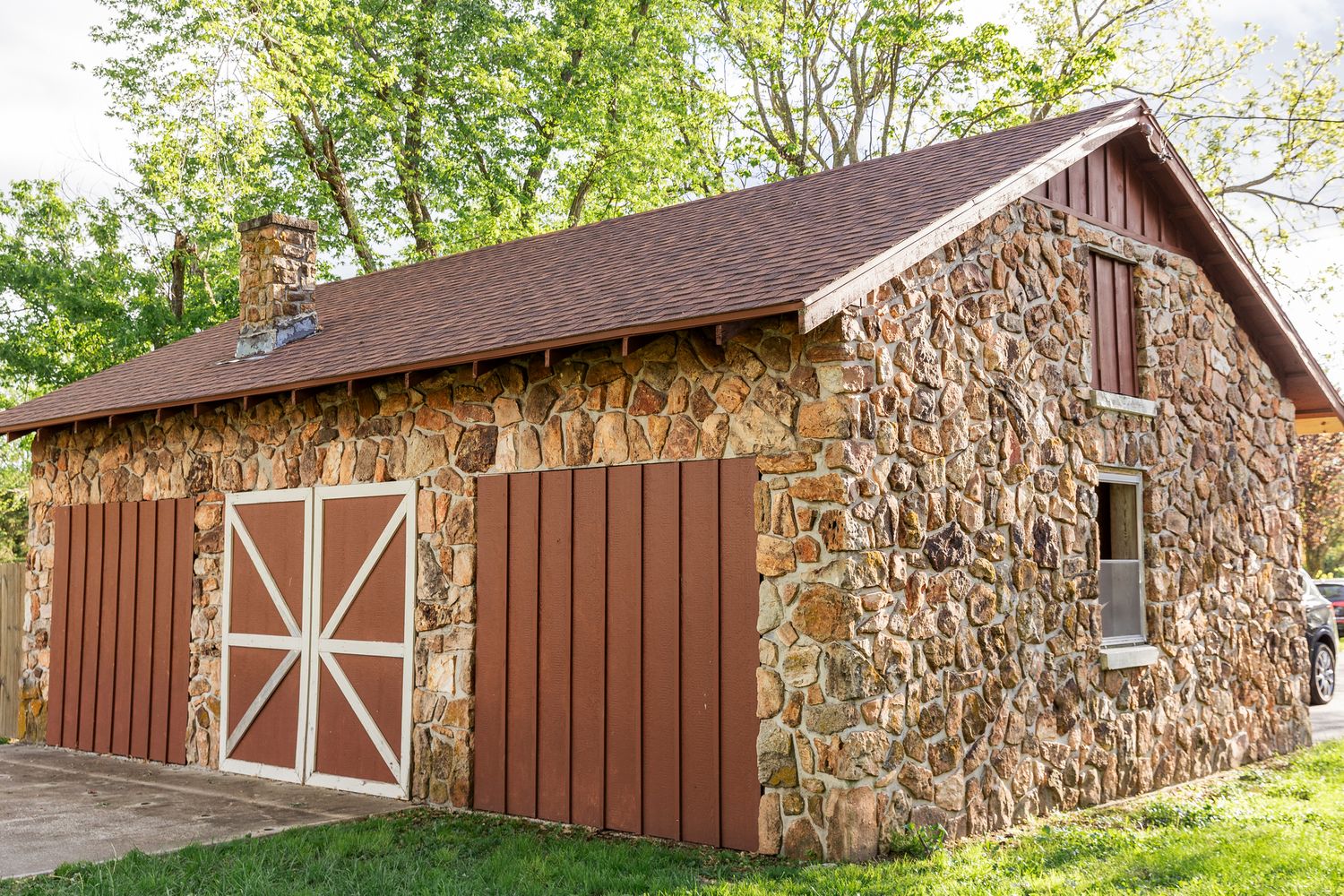 Stone and wood barn buildings with brown siding and white trim in a countryside setting.