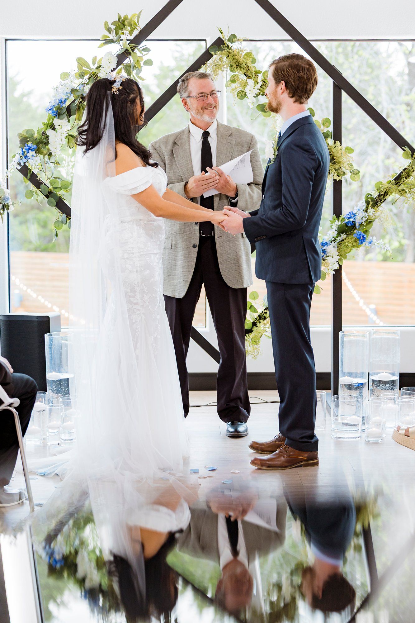 A wedding ceremony takes place under a floral arch with a couple exchanging vows in front of an officiant.