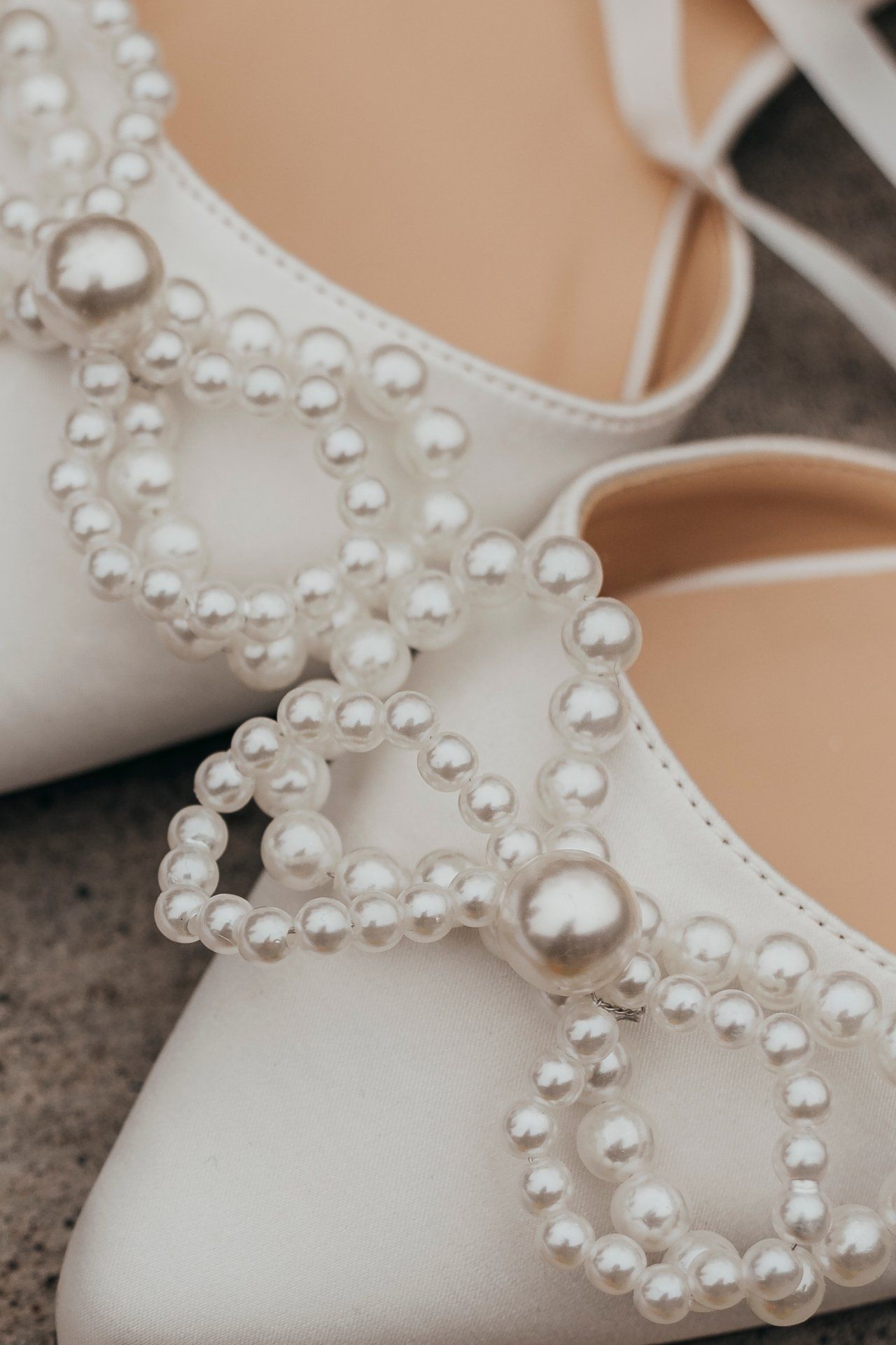 Close-up details of a white bridal shoe decorated with delicate pearl embellishments arranged in floral patterns.