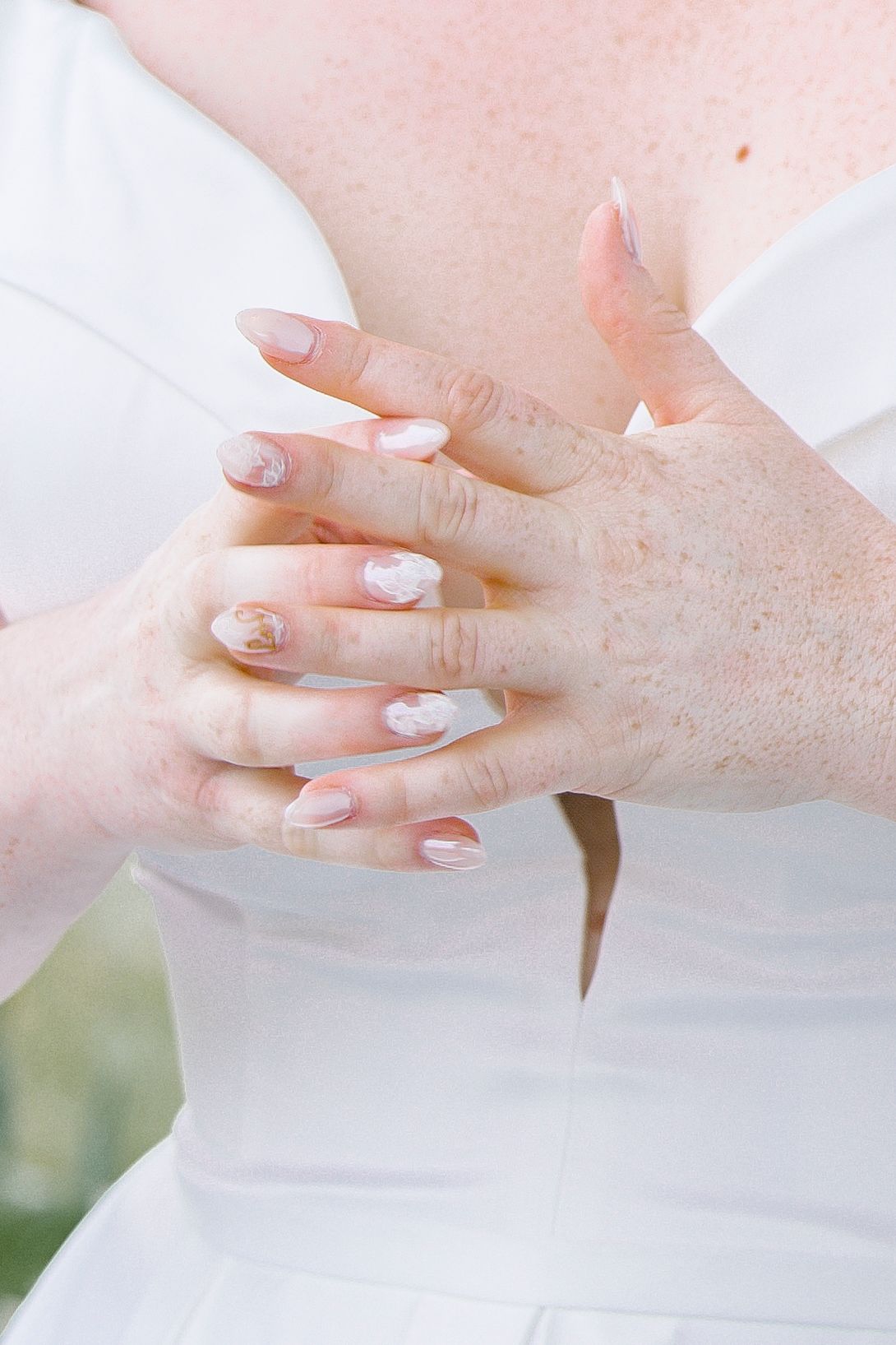 Close-up of bridal hands with French manicure and white wedding dress details.