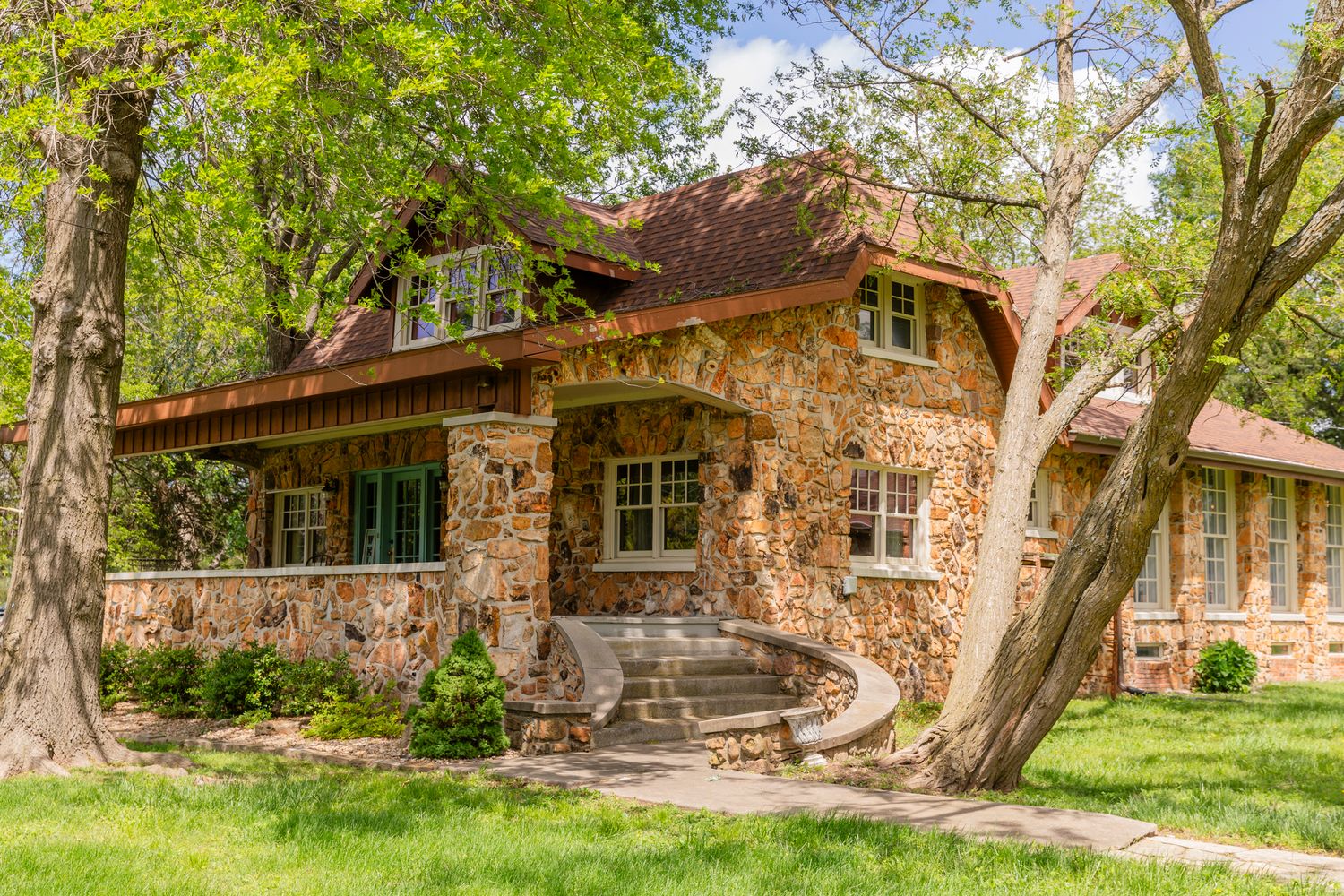 Charming stone cottage with curved stone steps features rustic architecture surrounded by mature trees in a peaceful setting.