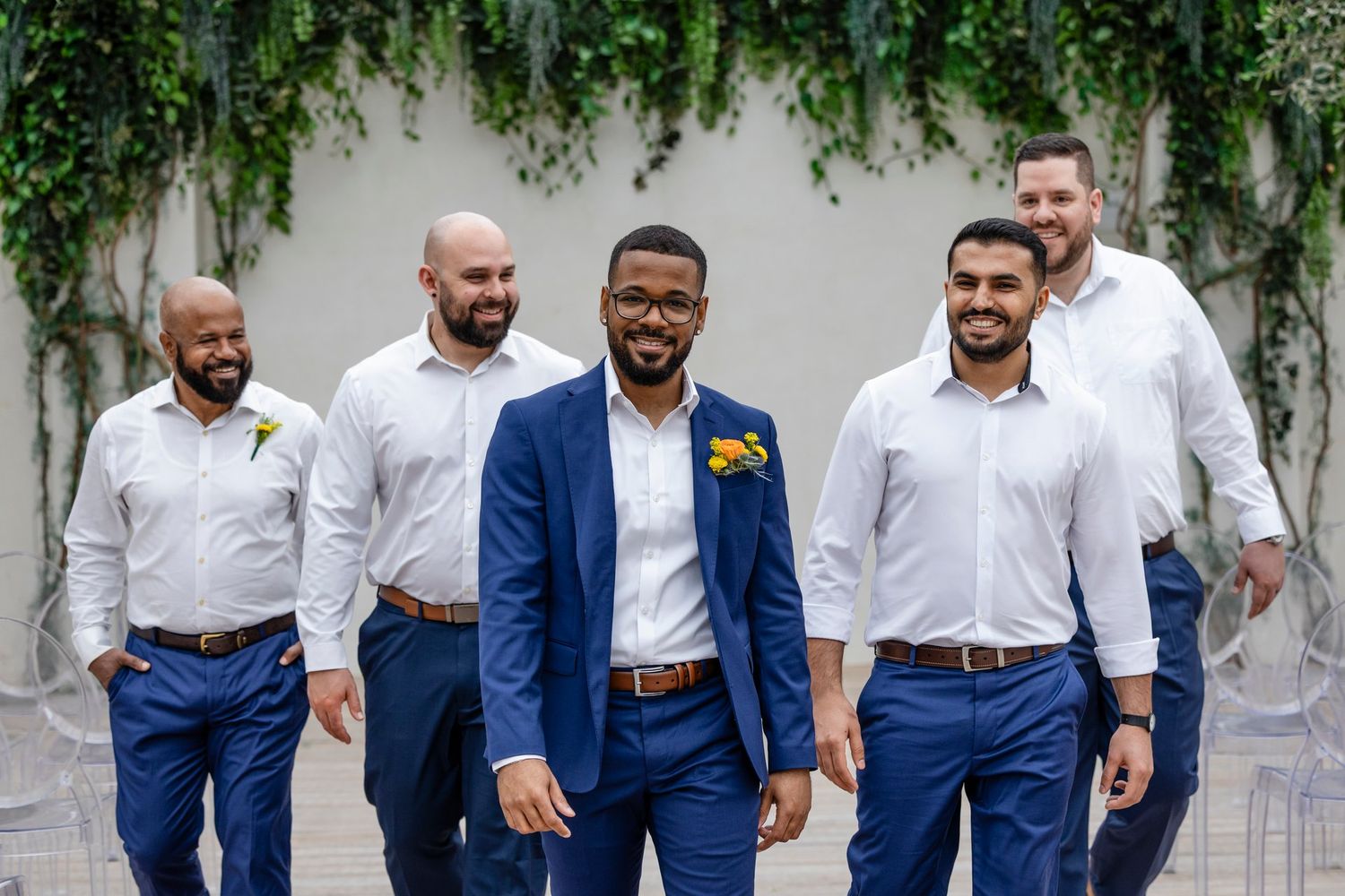 Group of five groomsmen in coordinated outfits with navy blue pants and white shirts standing outdoors.
