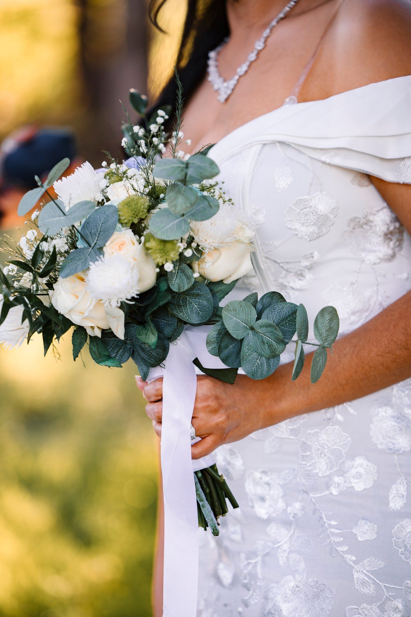 Close-up of elegant bridal bouquet featuring white roses and eucalyptus leaves against a lace wedding dress.