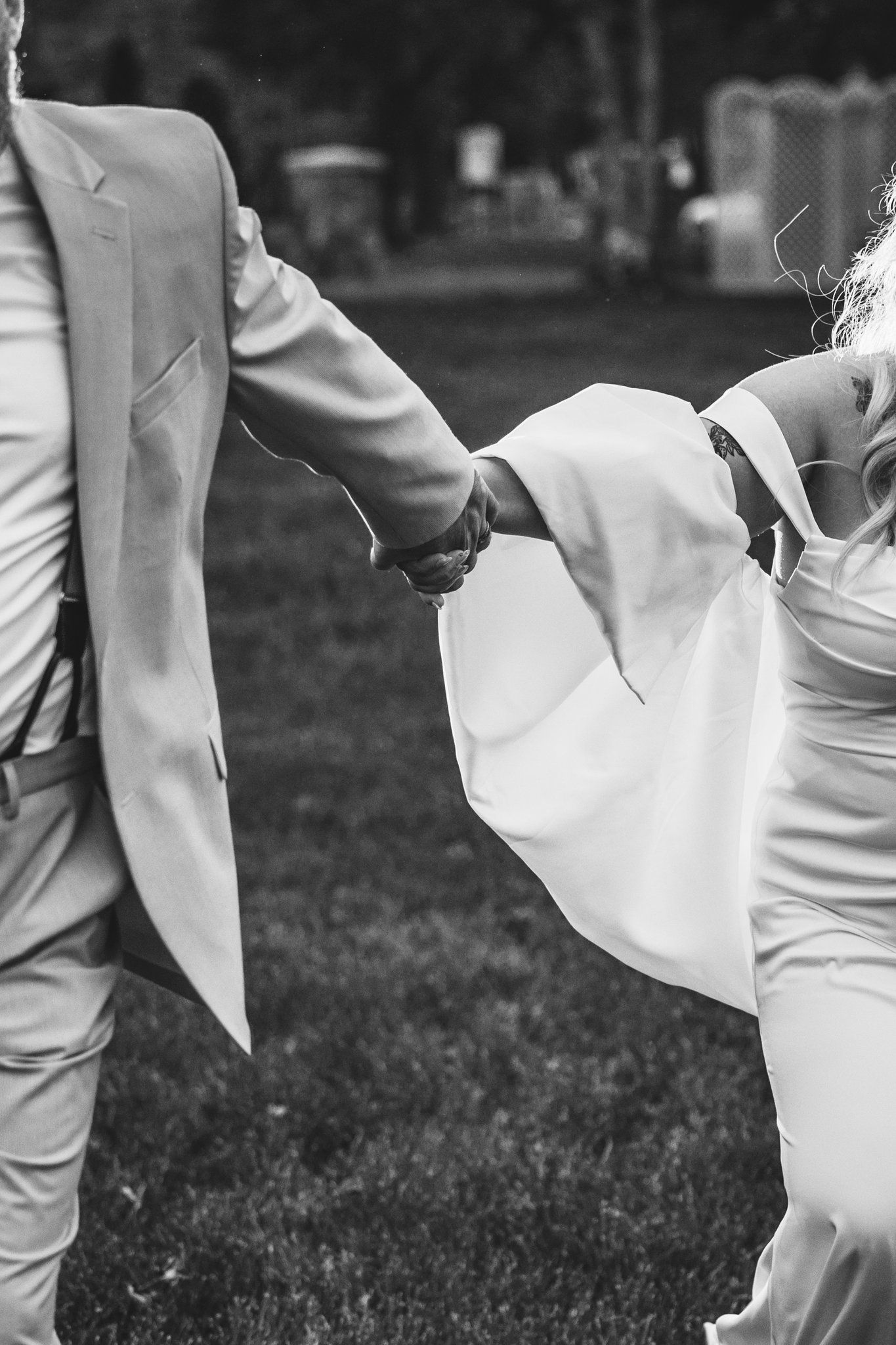 Black and white photo of couple in wedding attire standing on grass with woman dipping while holding hands.