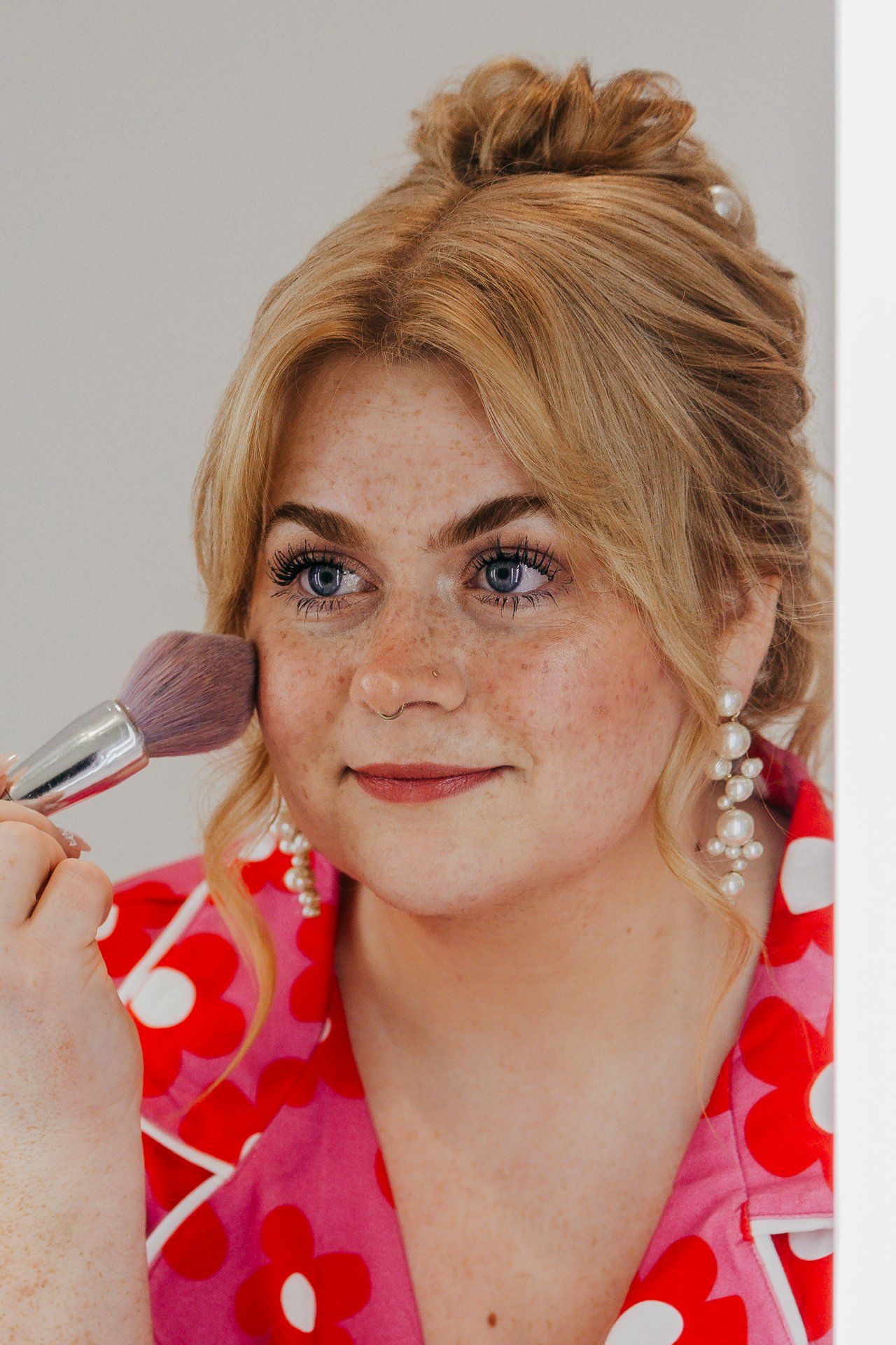 Makeup artist applying blush with brush on model wearing red floral dress.