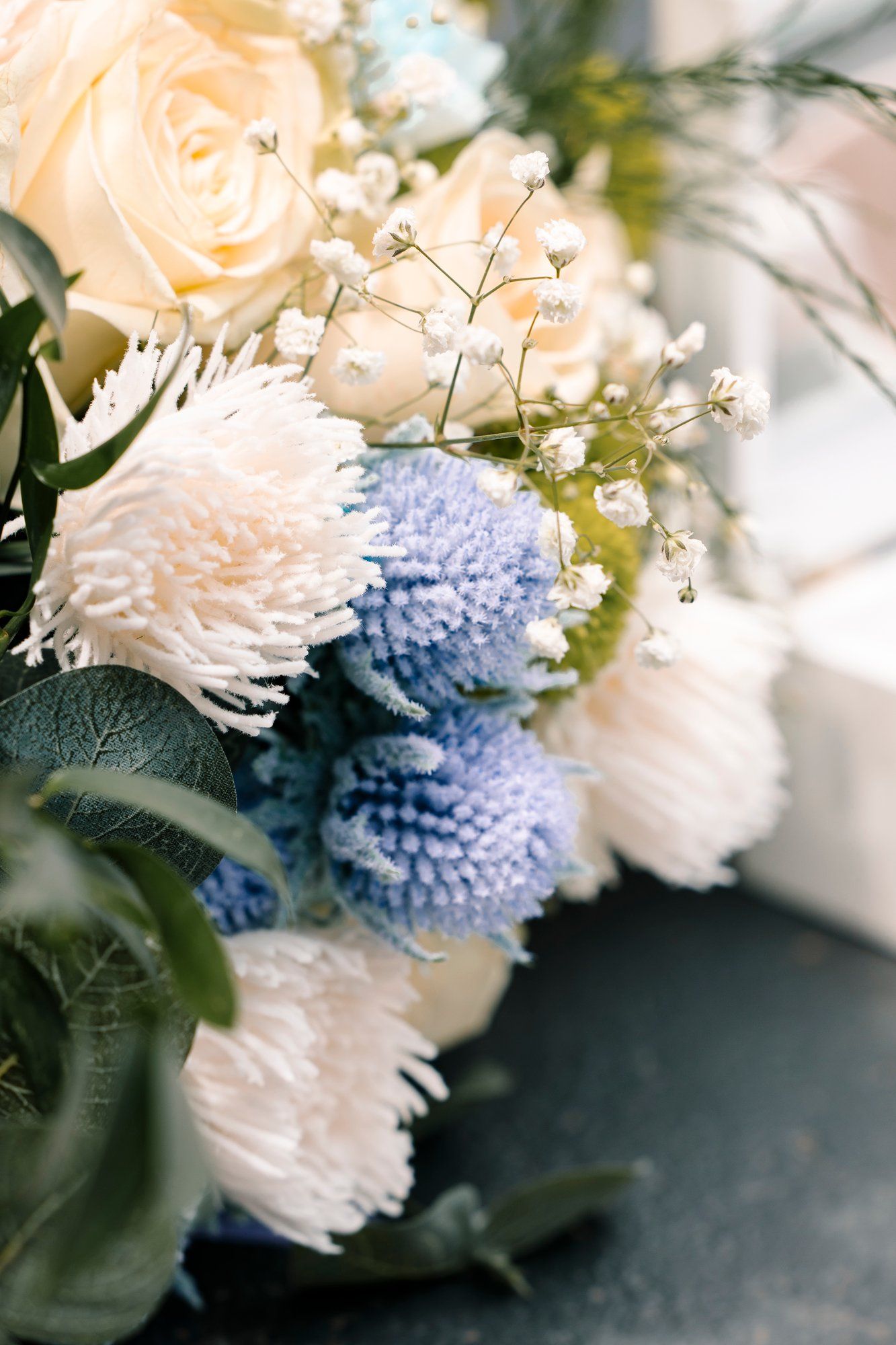Delicate floral arrangement featuring white chrysanthemums and light blue button poms against a dark background.